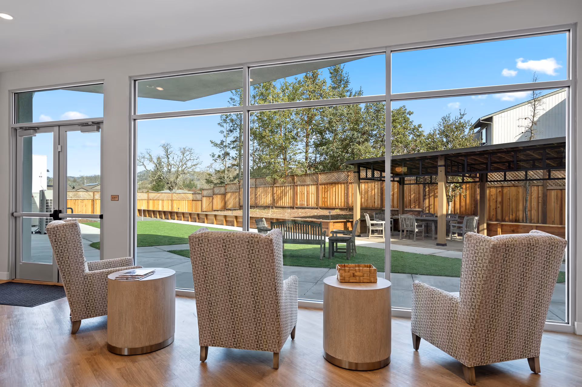 Bright interior lounge with four patterned armchairs and round tables beside a large window.
