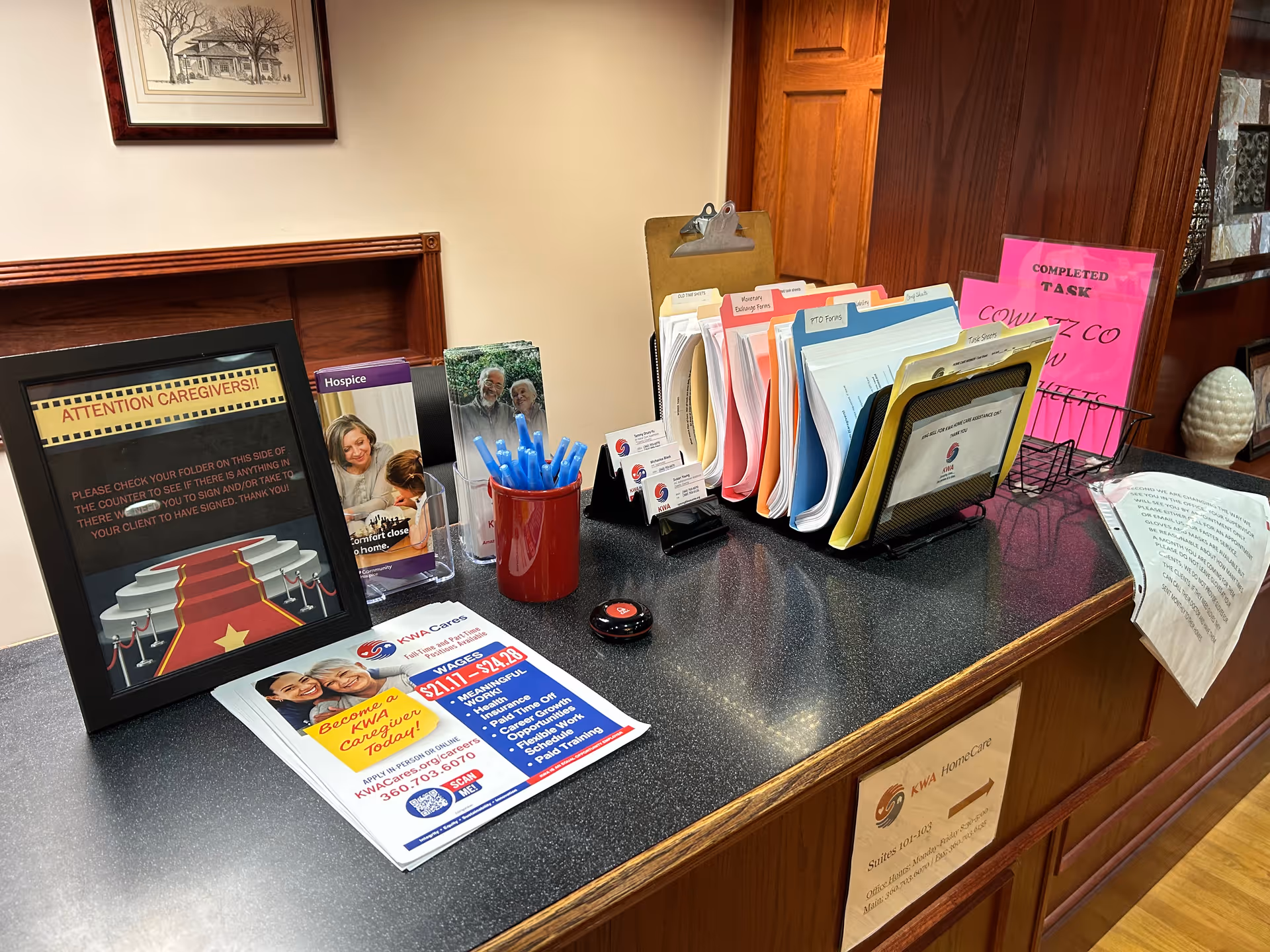 A senior care reception desk with folders, brochures, pens, and a framed poster.