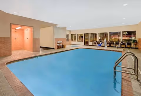 Indoor swimming pool with tiled deck, pool lift, seating and large windows in a facility.