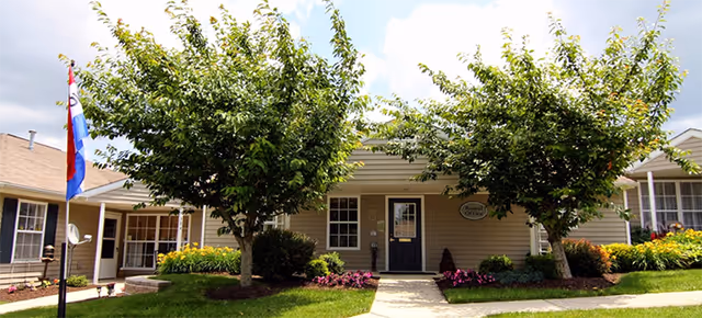 Front exterior of a senior living facility with two trees, walkway, and entrance.