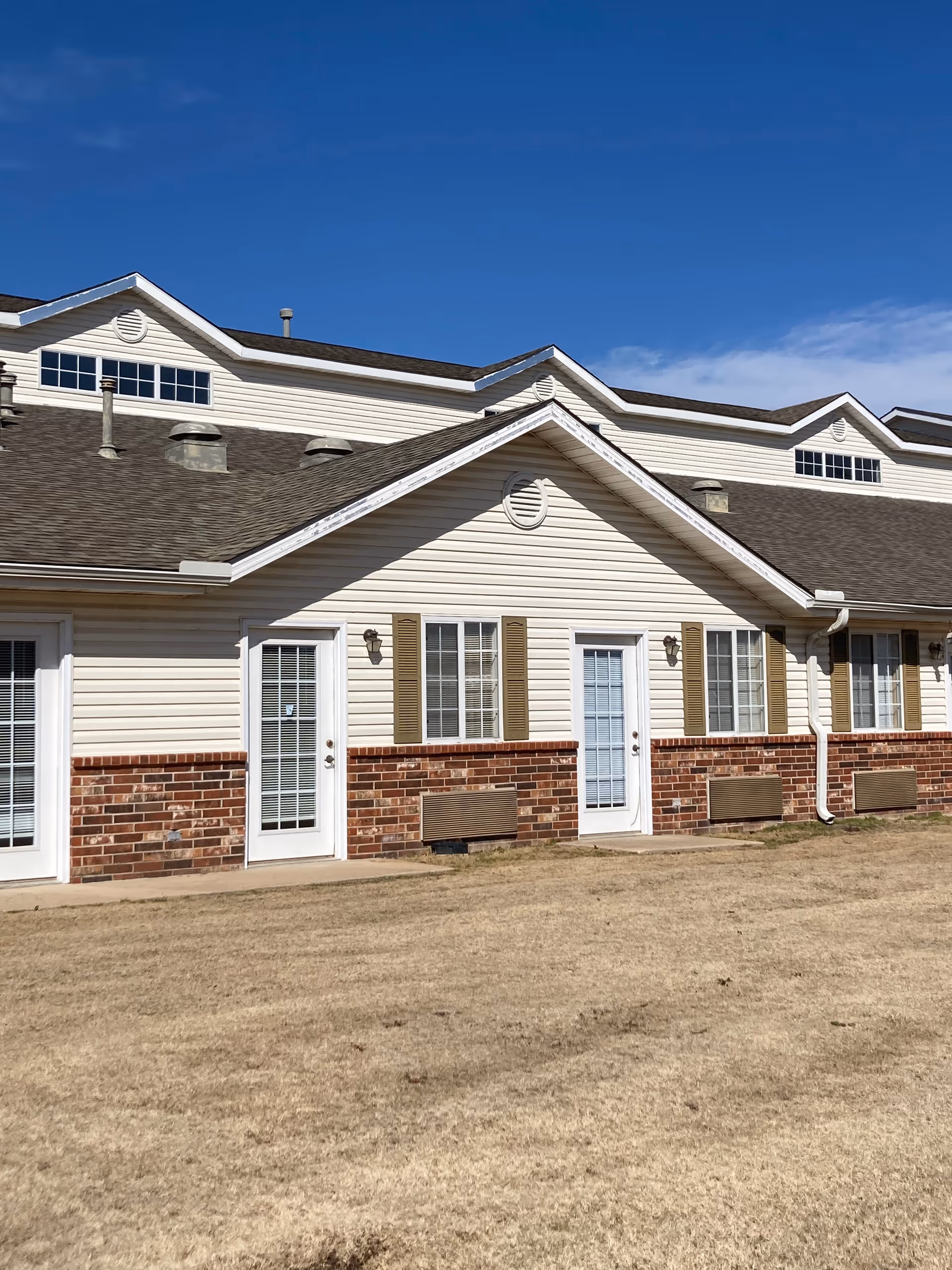 Exterior view of a senior living facility with brick accents and white doors.