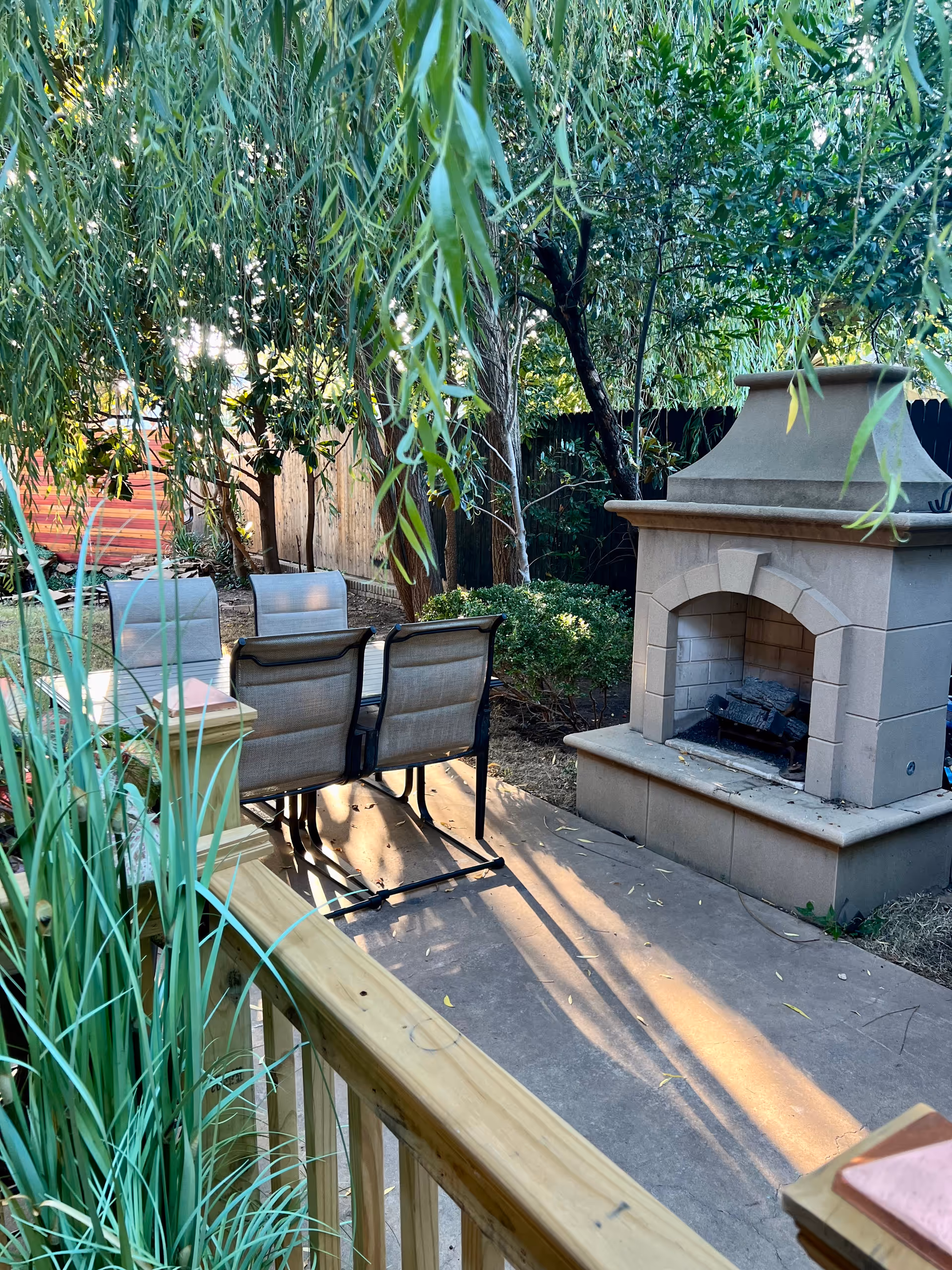 Outdoor patio with four chairs around a stone fireplace among lush trees