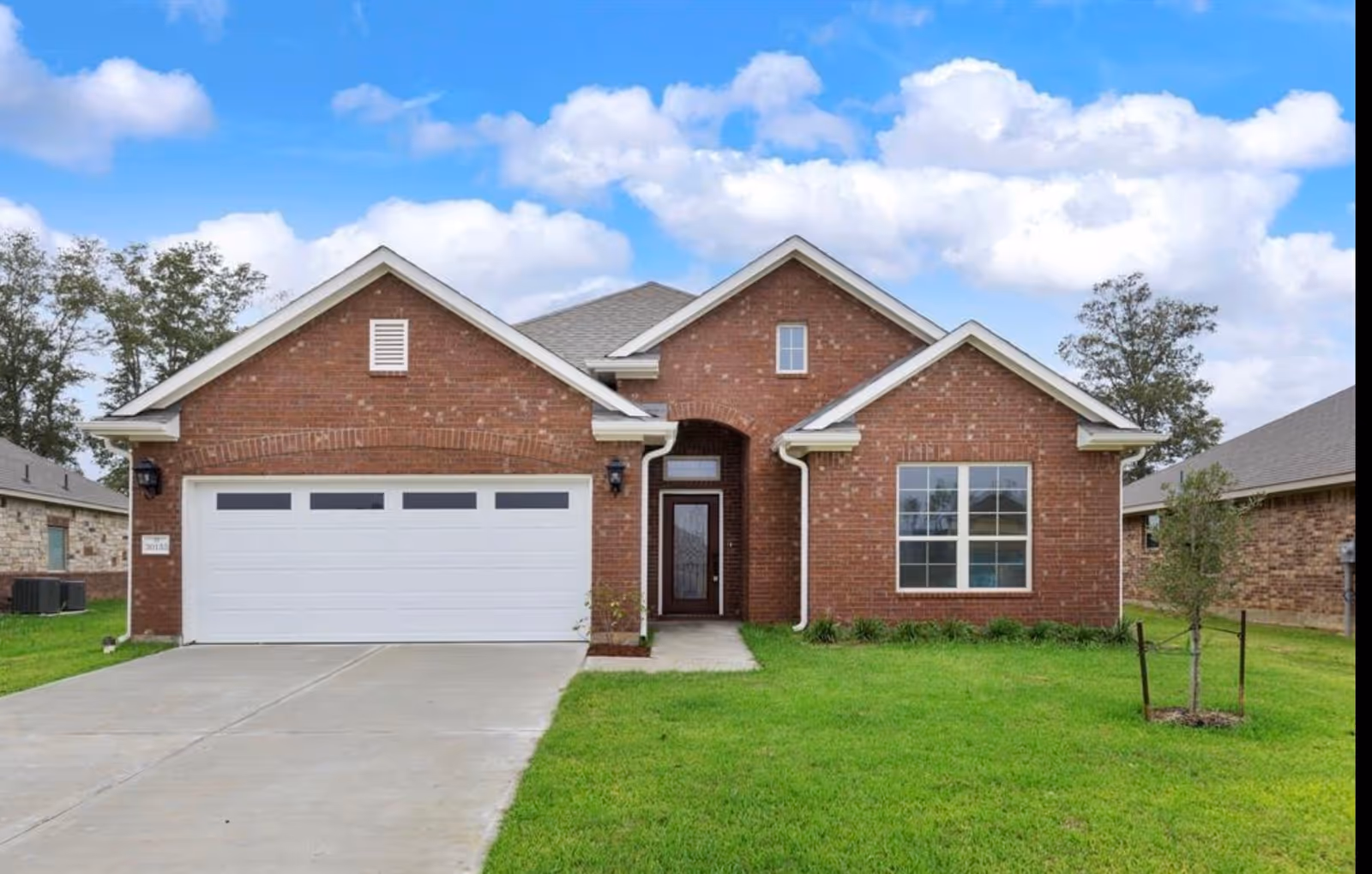 Front view of a brick house with a white two-car garage and green lawn.