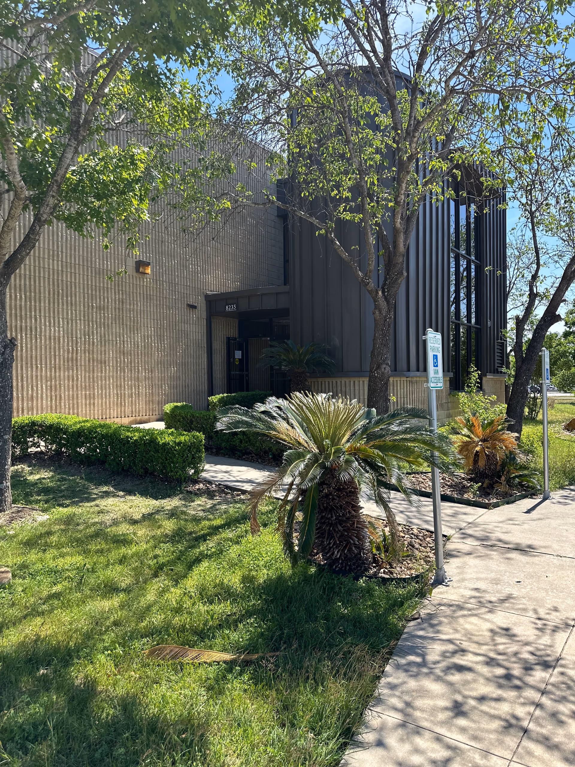 Exterior view of a building entrance with trees and a sidewalk.