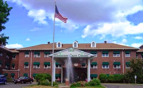 Exterior view of Ebenezer Care Center building with flagpole, fountain, and front entrance.