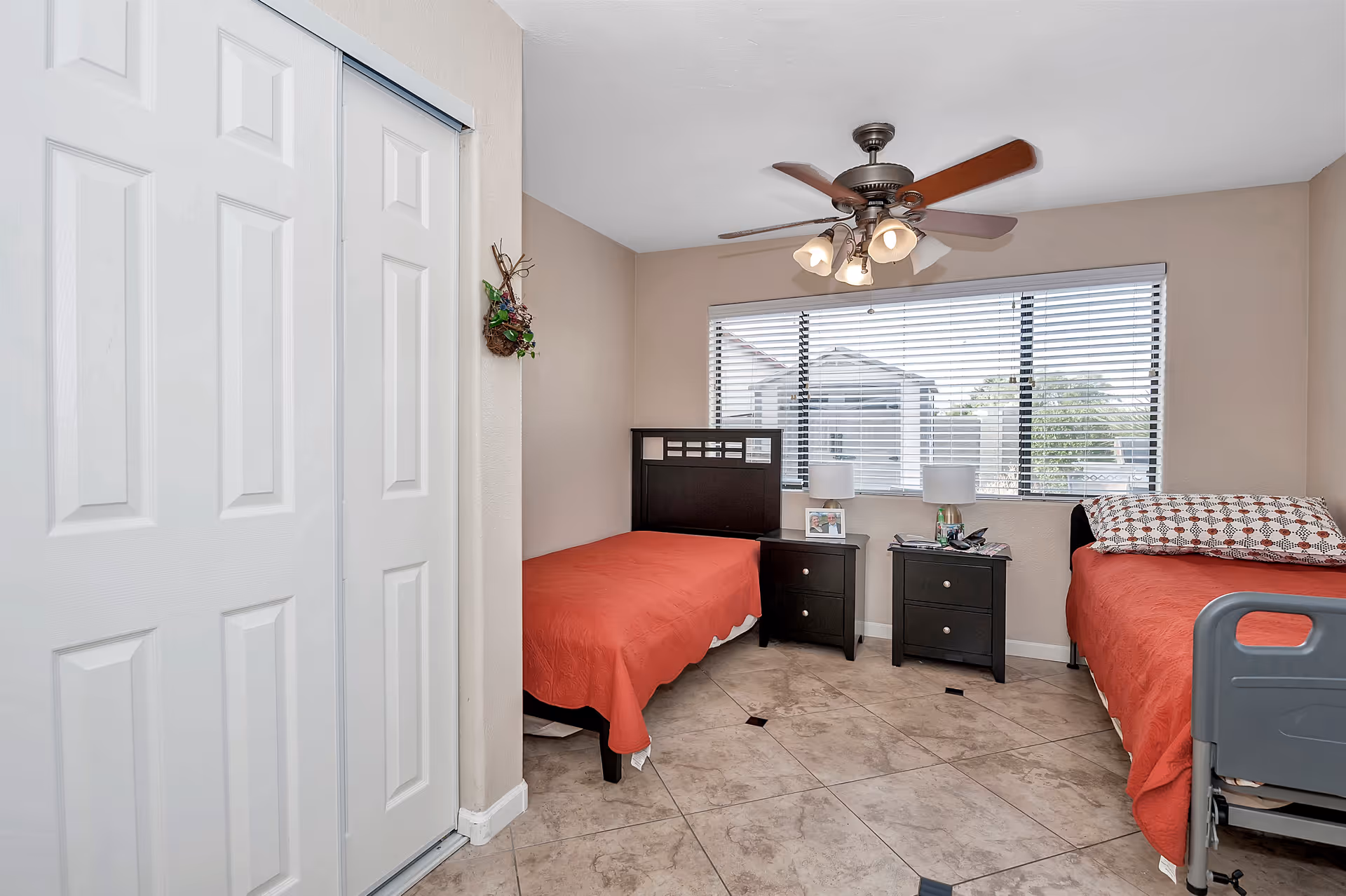 Two twin beds with red bedspreads, matching nightstands, and a ceiling fan in a beige bedroom.