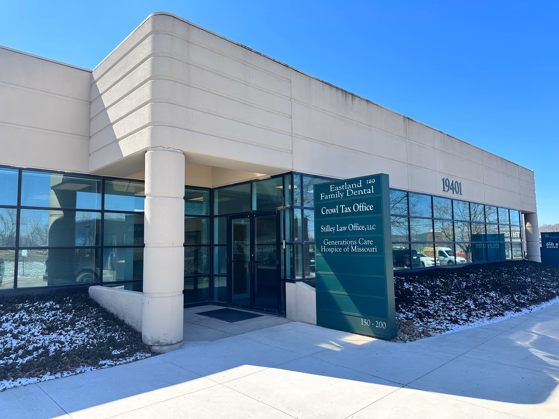 Modern office building entrance with glass storefront and a tall green tenants sign.
