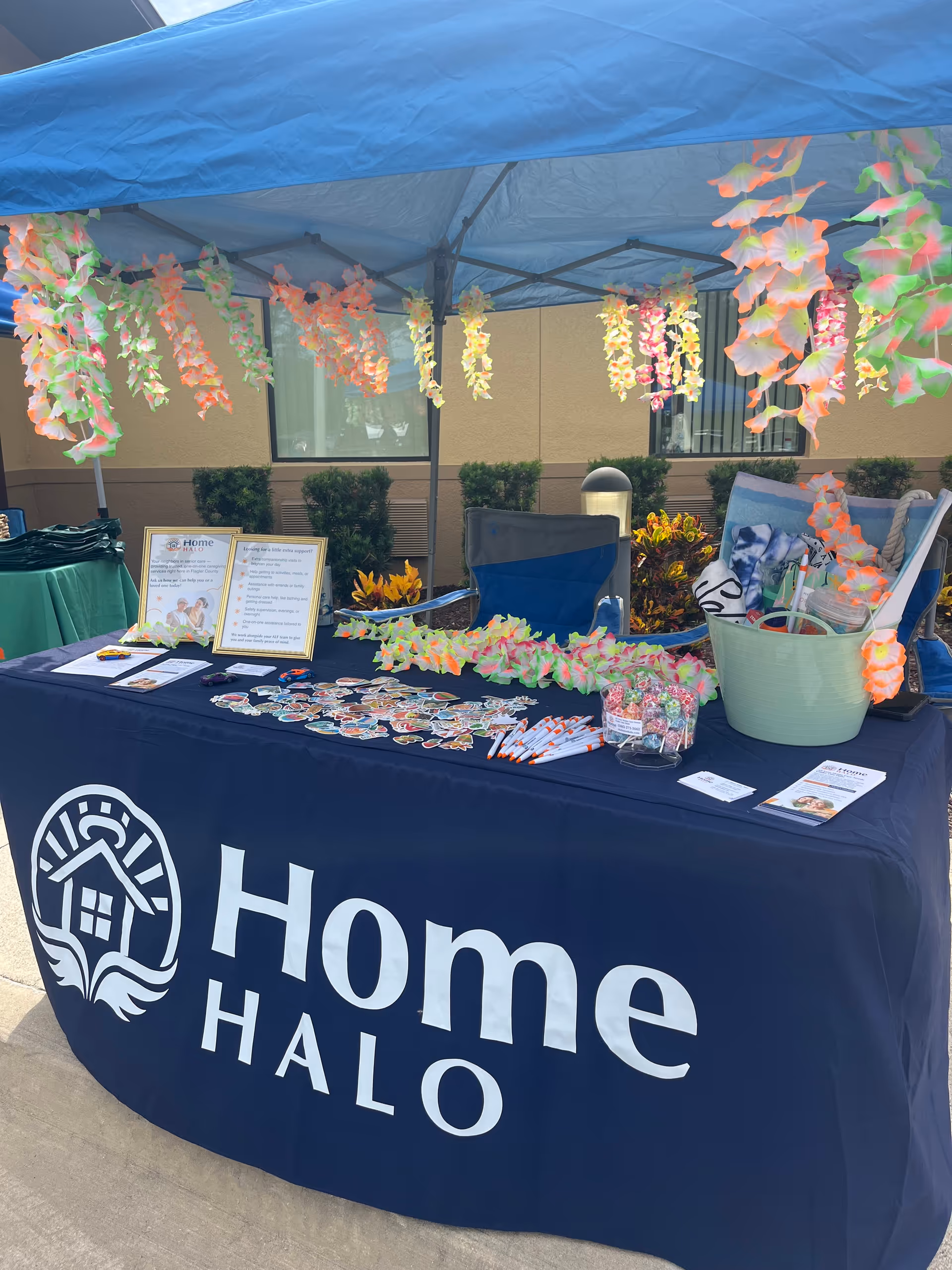 Outdoor promotional booth for Home Halo with table, leis, and informational materials under a blue canopy.