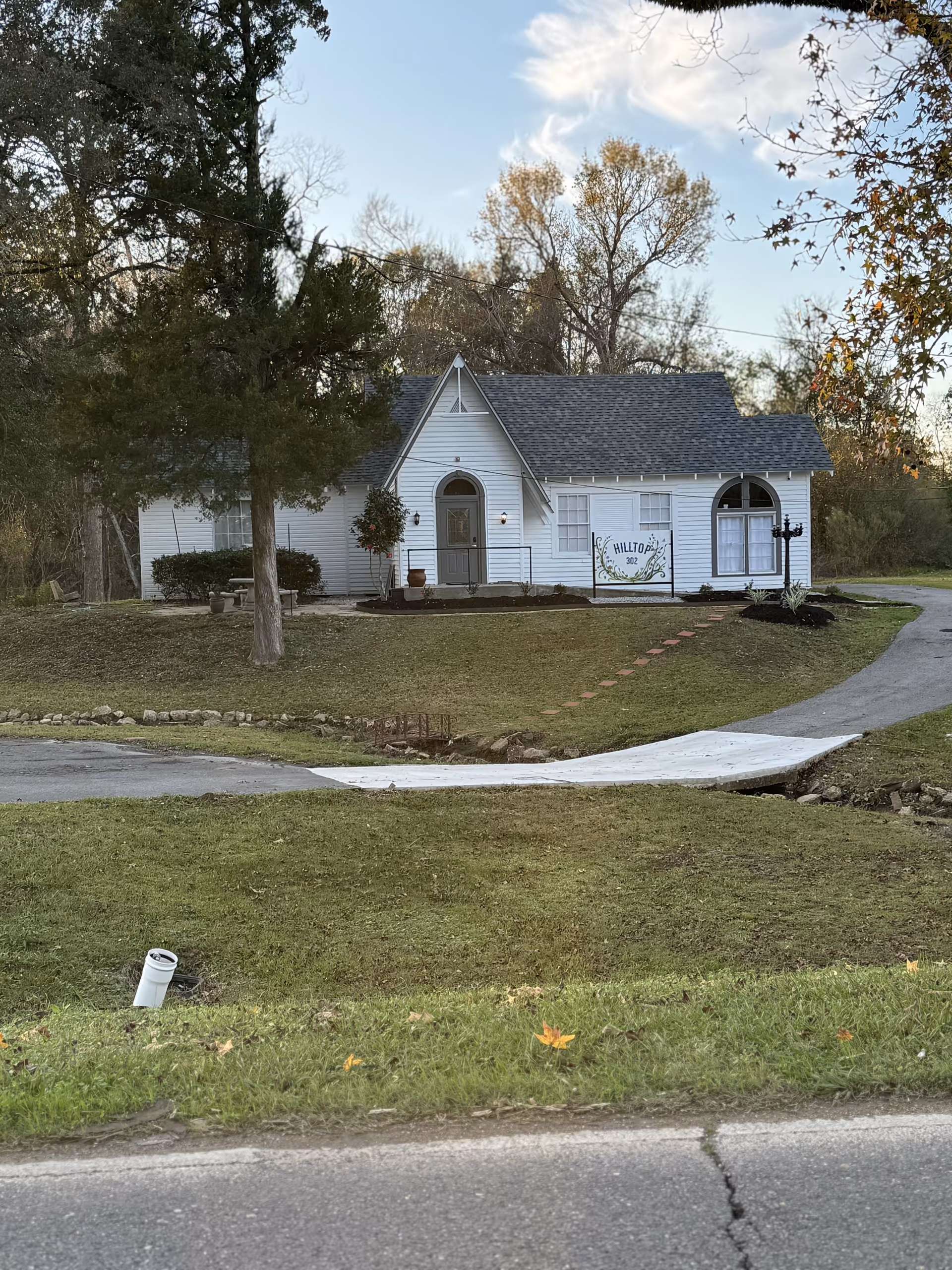 White cottage-style senior living facility with front entrance, sign, drive, and manicured lawn.
