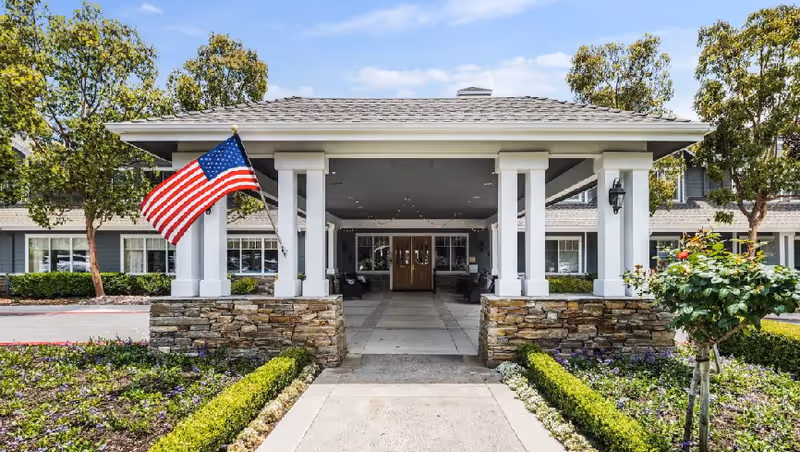 Front entrance of Eastwood Cottage I senior living facility with flag and landscaped walkway.