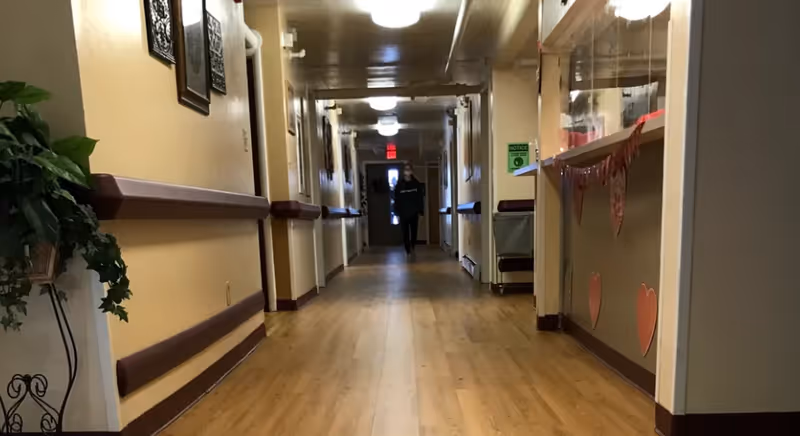 A long interior hallway at Arbor Village, with a person walking toward the camera.