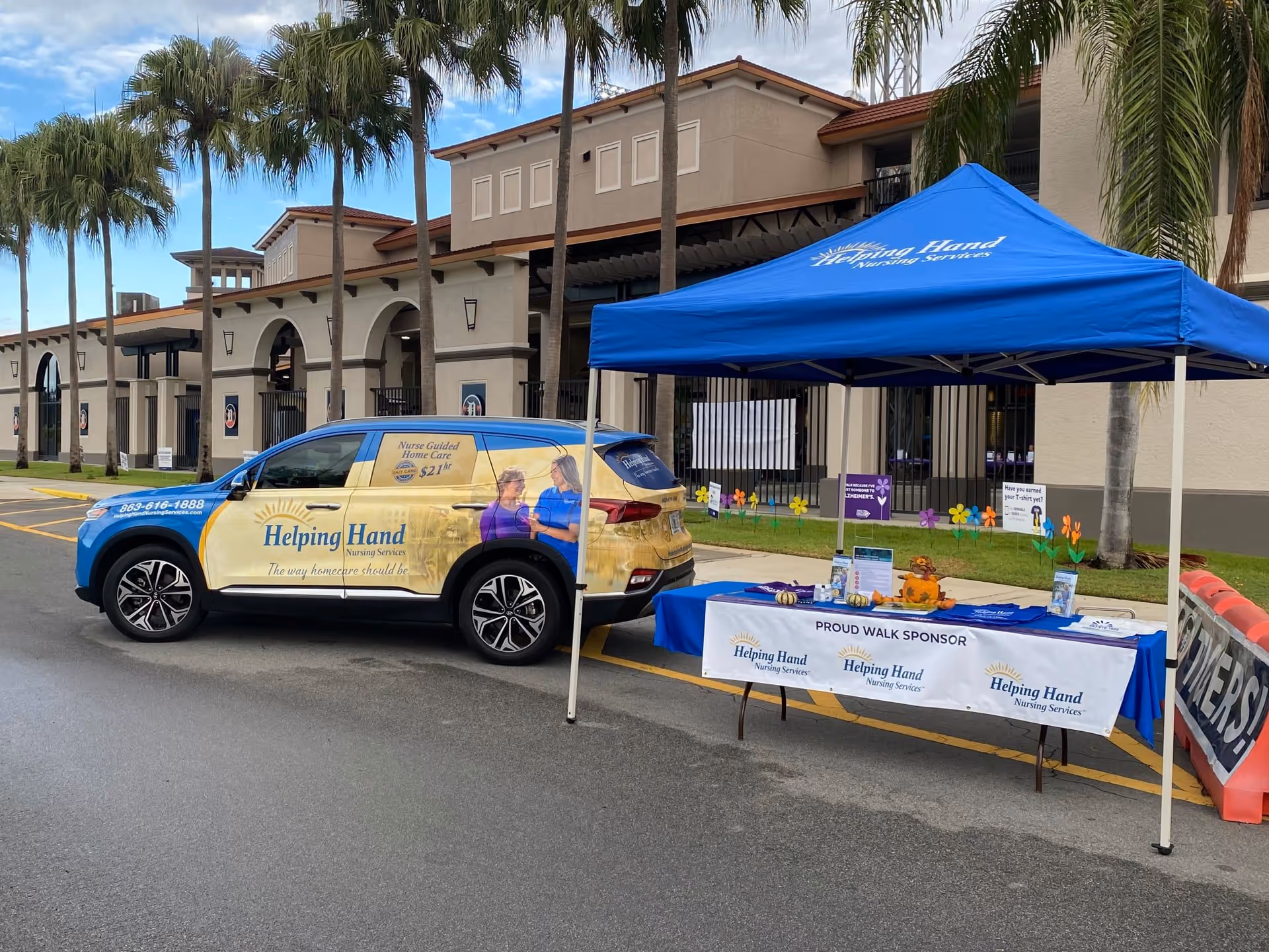 Blue canopy tent and promotional table setup outside Helping Hand Nursing Services facility.