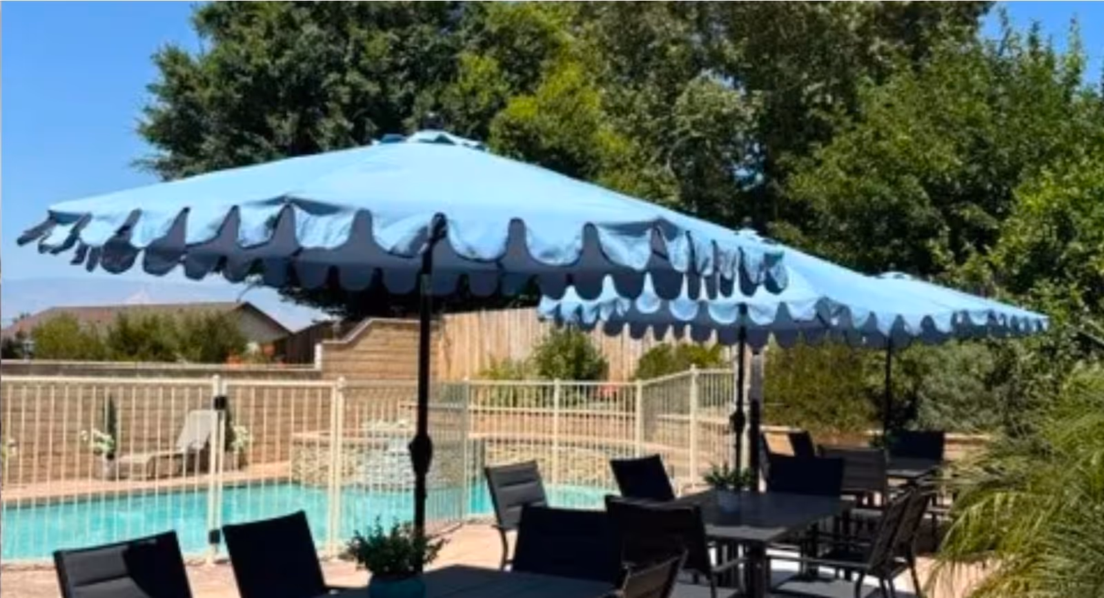 Blue umbrella shades an outdoor patio beside a fenced pool at Birch Residence.
