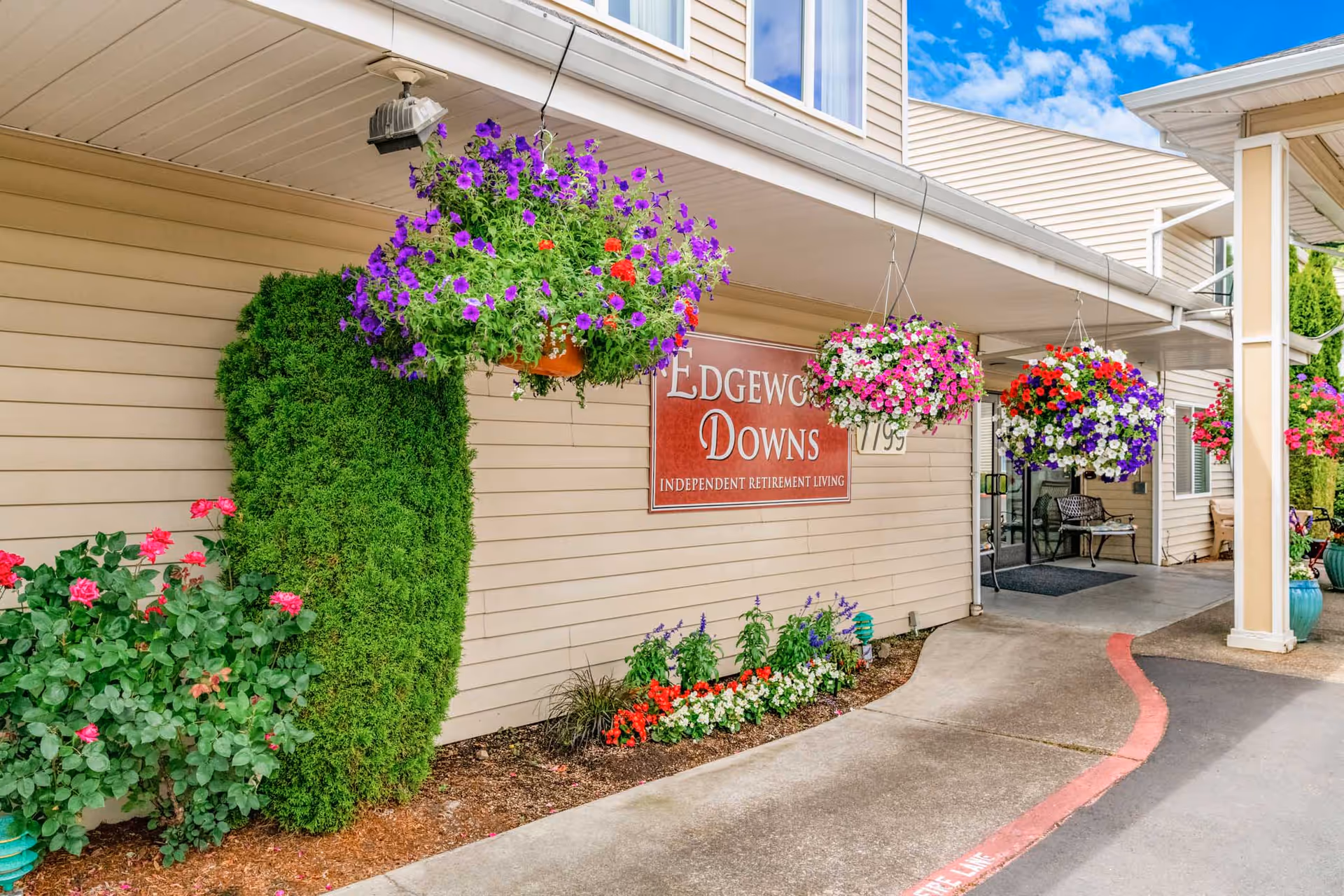 Covered entrance to Edgewood Downs independent retirement living with hanging flower baskets and landscaped beds.