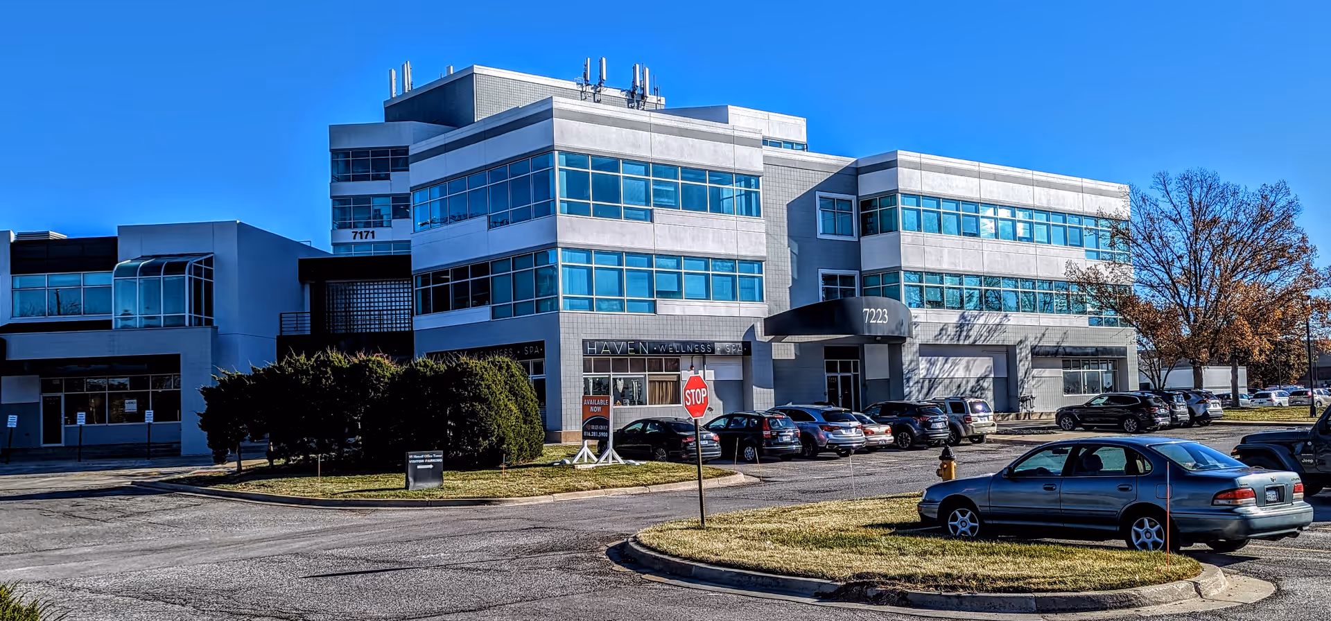 Modern three-story healthcare facility exterior with parked cars against a clear blue sky.