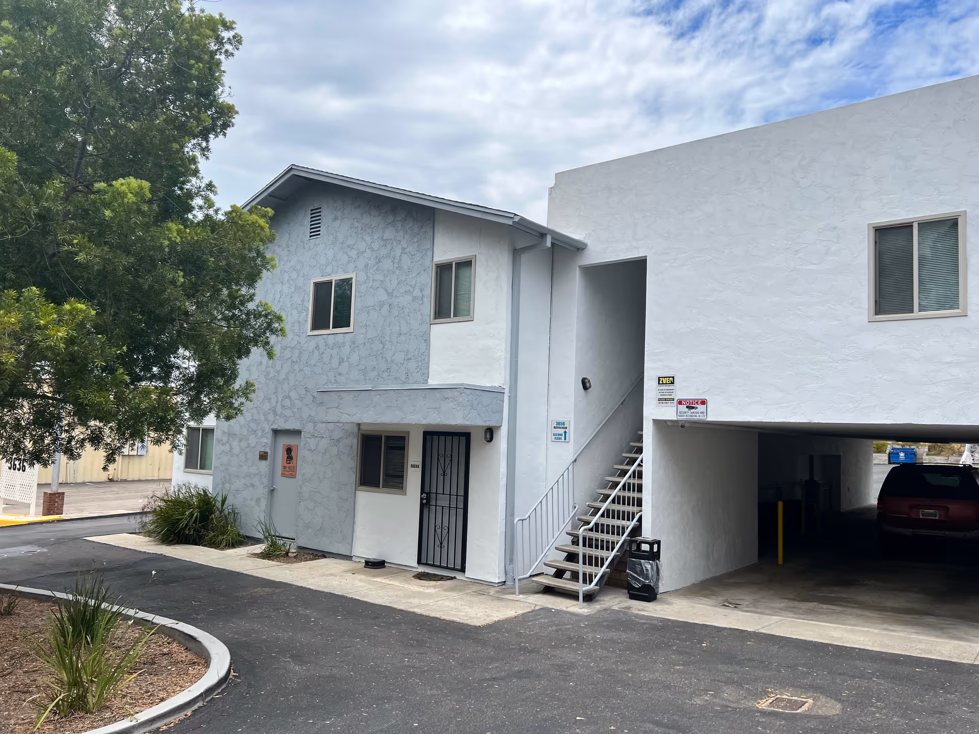 Exterior of a light-blue two-story senior facility with outdoor staircase and parking.