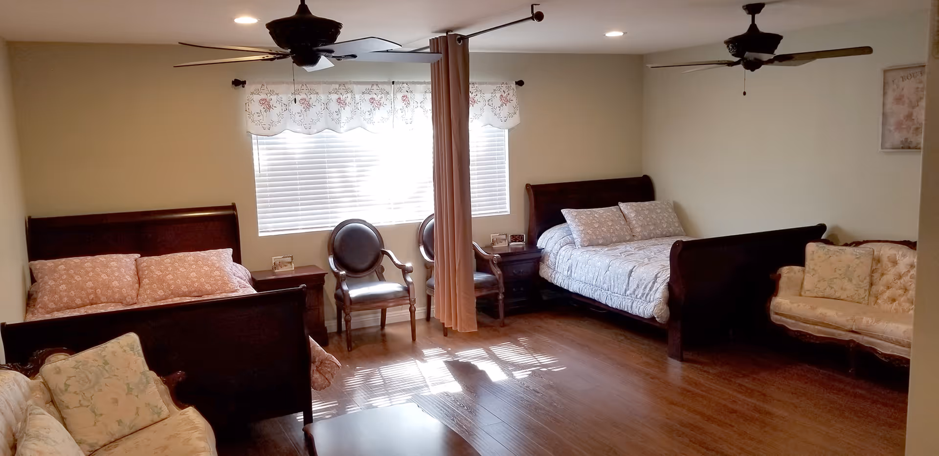 Spacious shared senior living bedroom with multiple beds, chairs, and a sofa.