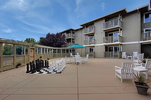 Outdoor patio of a senior living building with white chairs, giant chess set, and balcony units.