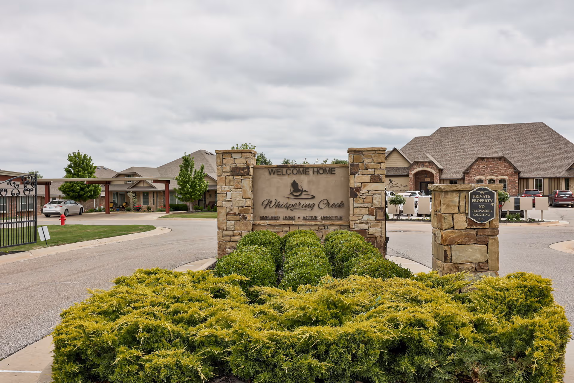 Stone entrance sign reads Whispering Creek, surrounded by green shrubs with buildings in the background.
