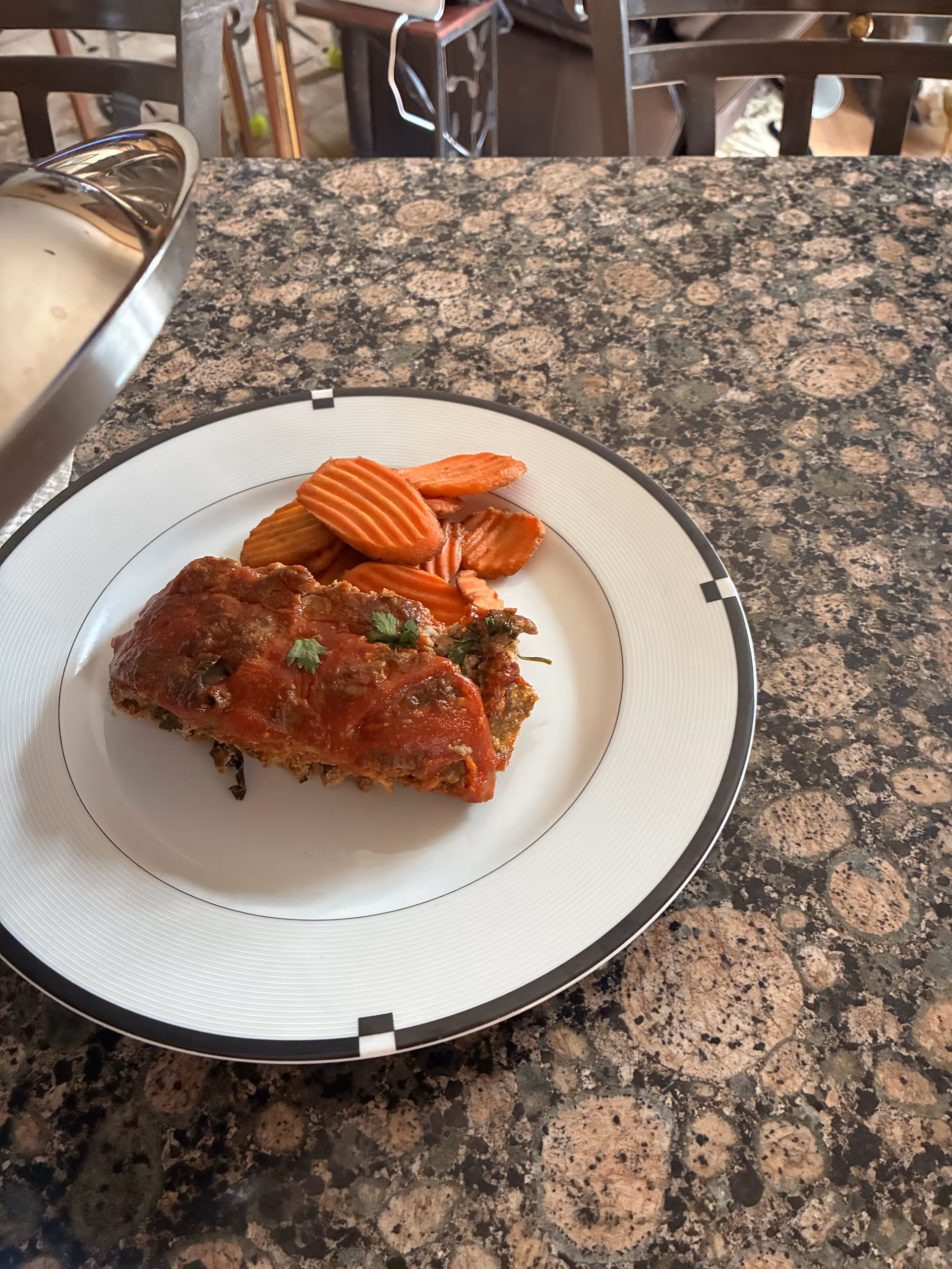 Plate of lasagna with potato chips on a granite dining table indoors.