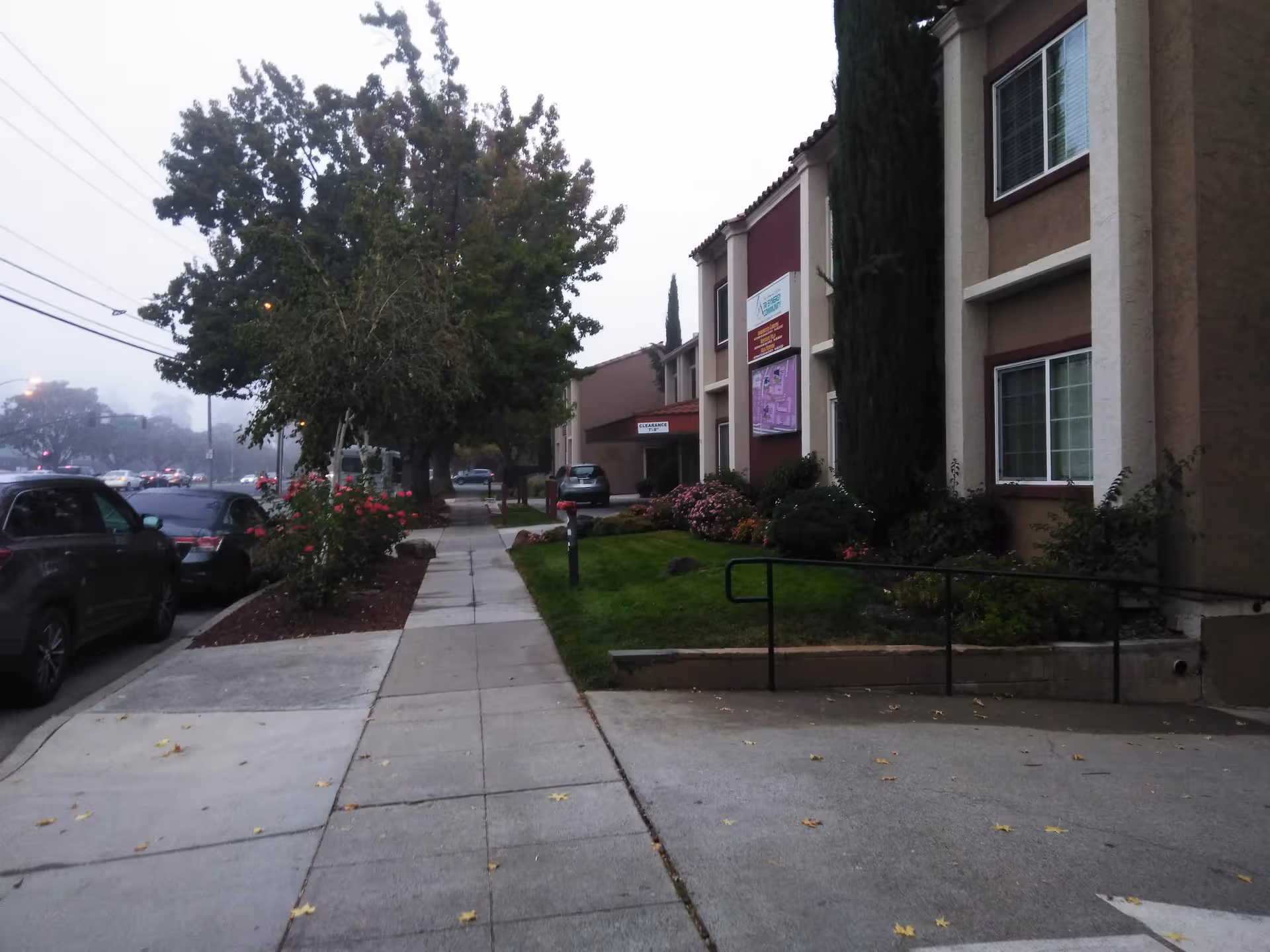 Exterior view of Villa Fontana Retirement Community with sidewalk, trees, and parked cars.