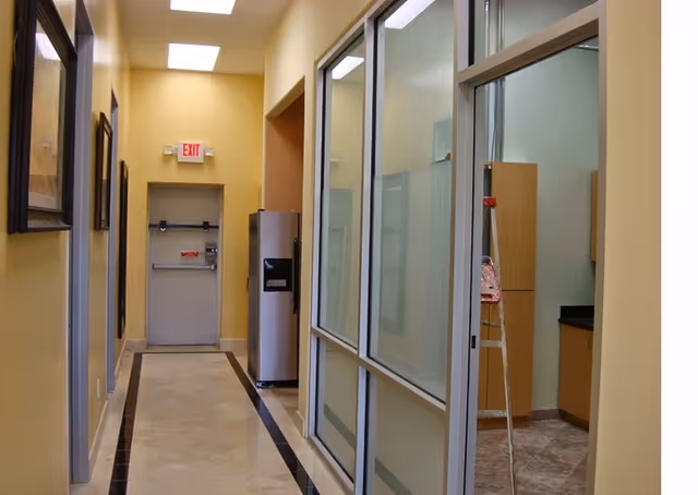 Bright hallway inside a senior living facility with glass partitions and an exit door.