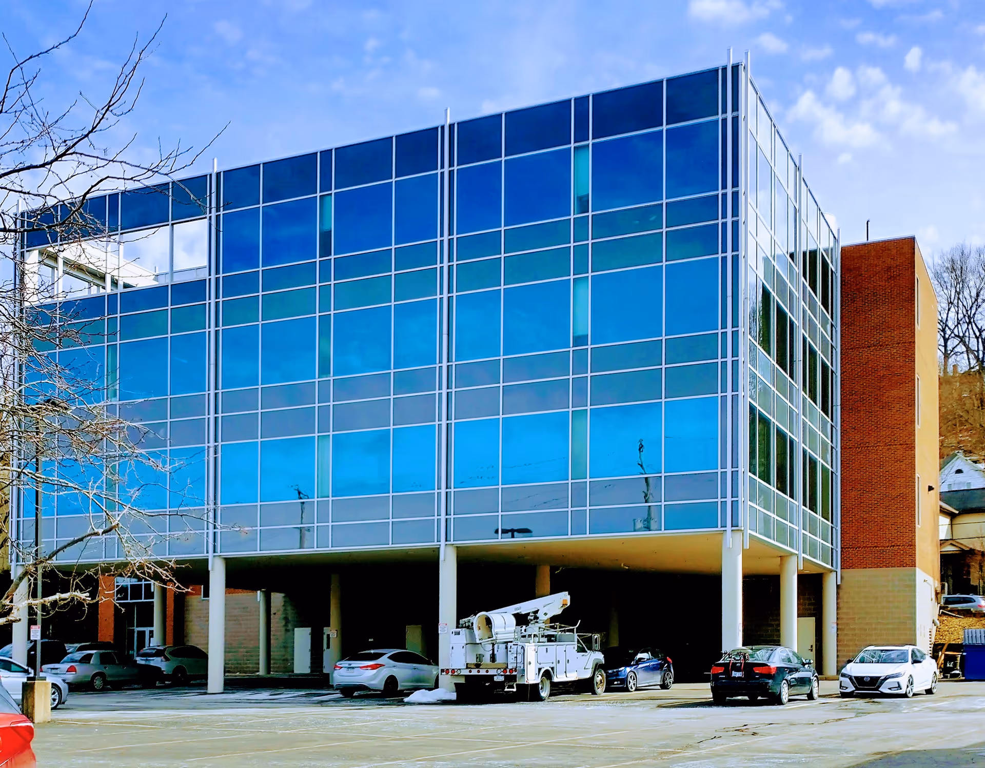 Modern glass-fronted building with blue-tinted windows and a parking area in front.