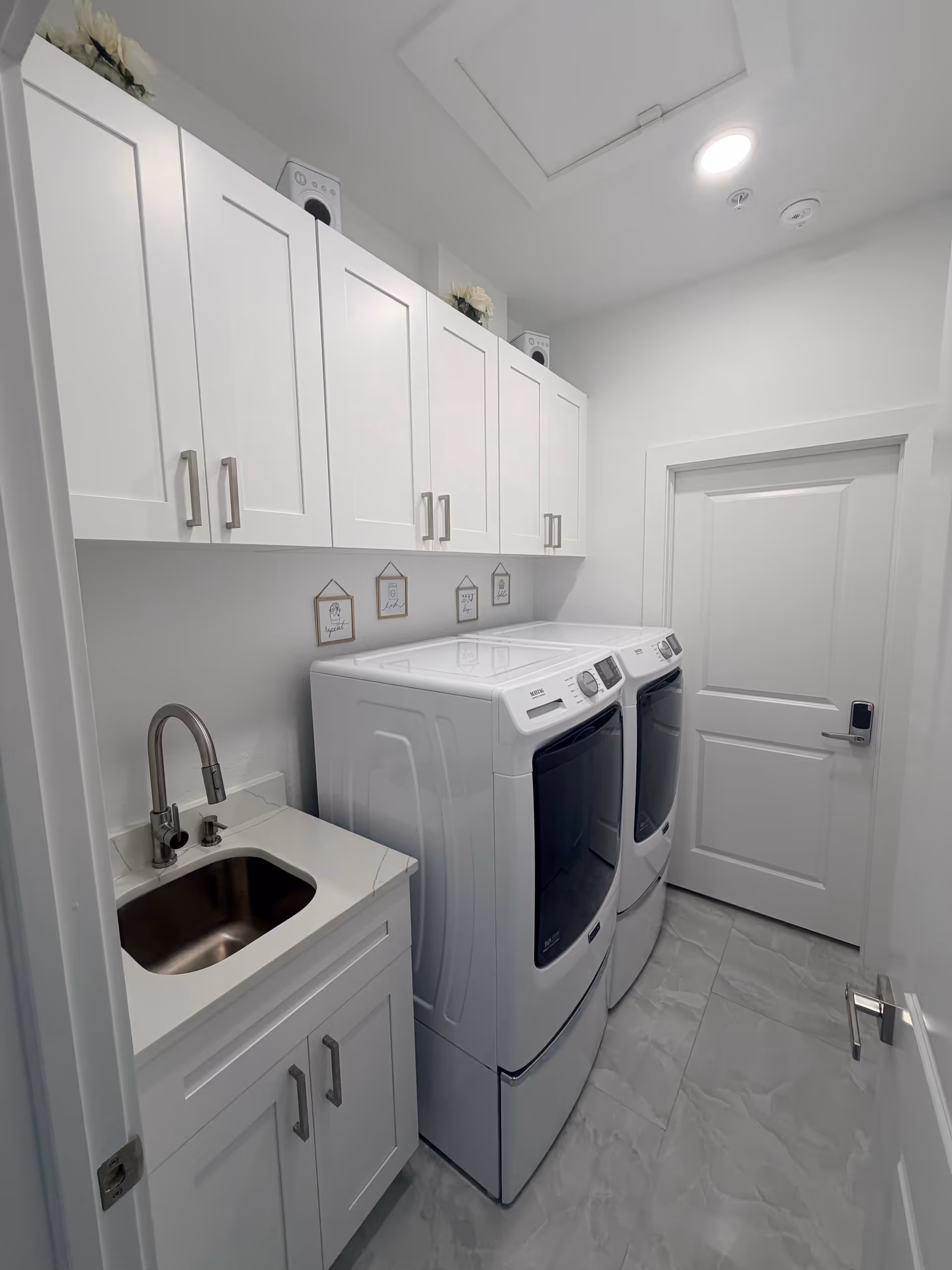 Bright white laundry room with stacked washer/dryer, sink, and tall cabinets.