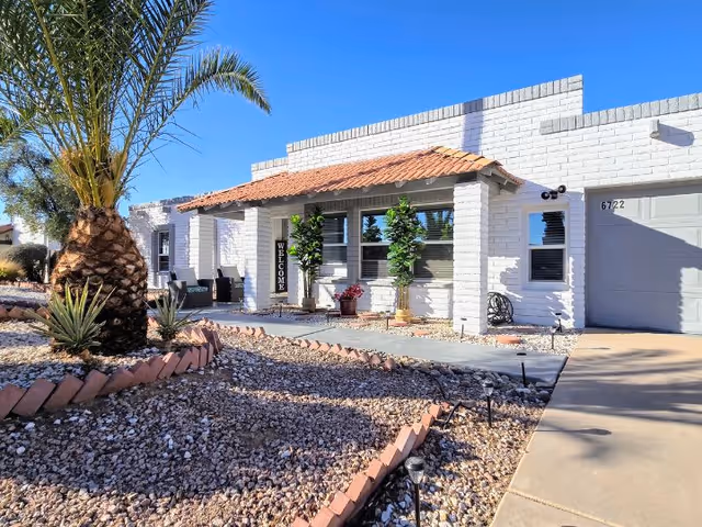 White brick senior living home with desert landscape and a palm tree at the entrance.