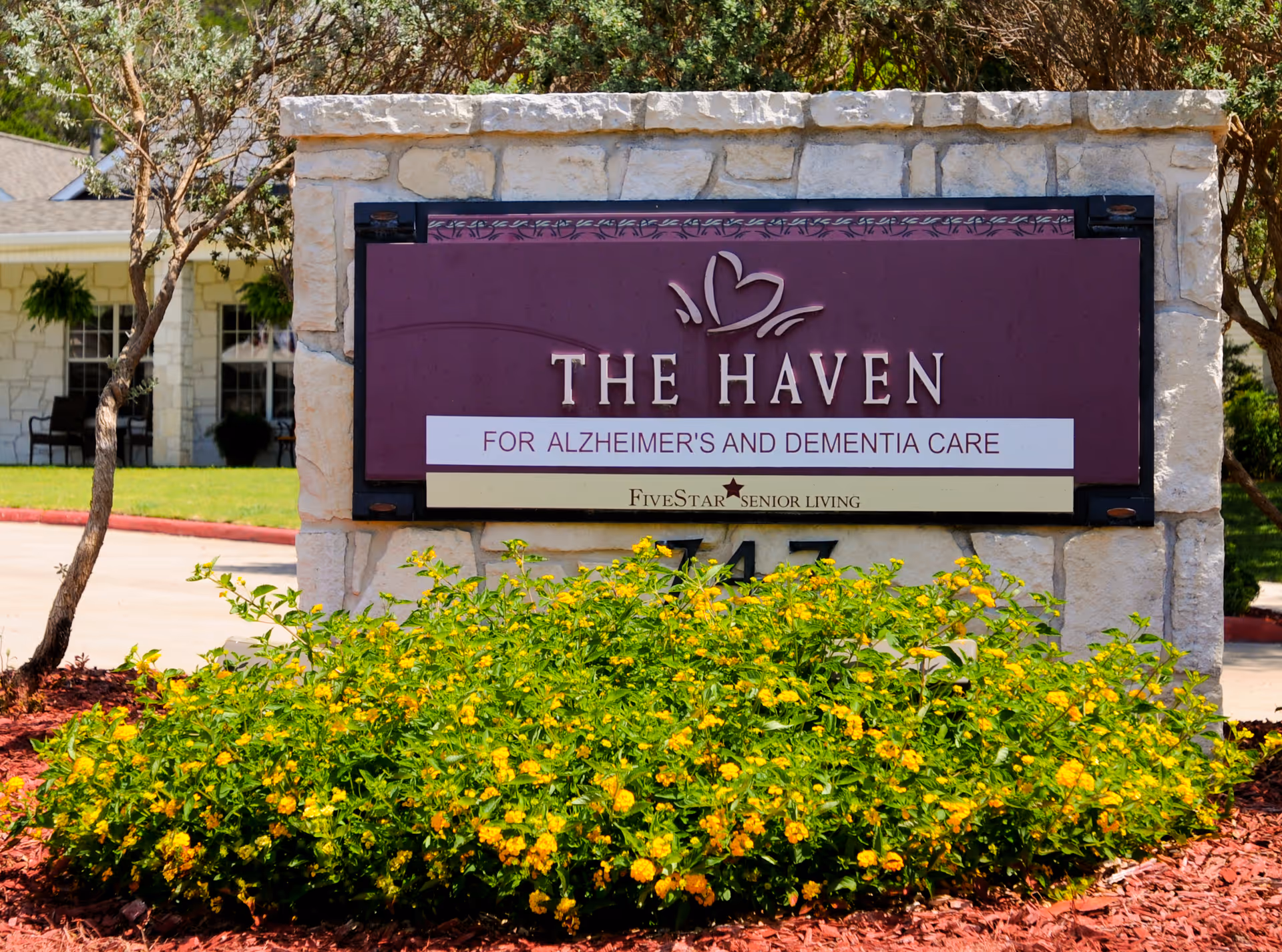Stone sign reads THE HAVEN FOR ALZHEIMER'S AND DEMENTIA CARE, with blooming yellow flowers in front.