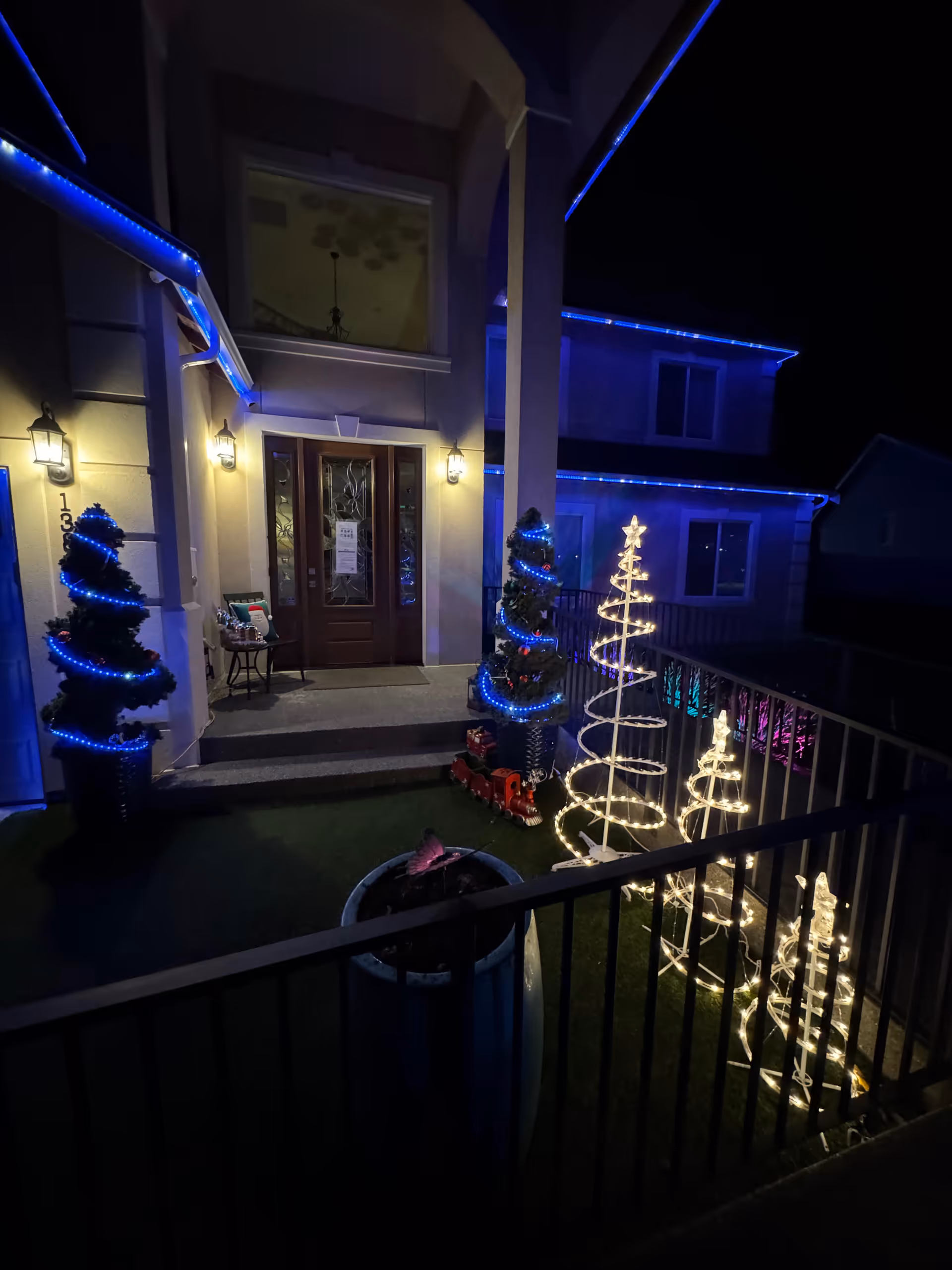 Front entrance of a house decorated with blue and white holiday lights and illuminated spiral tree decorations at night.