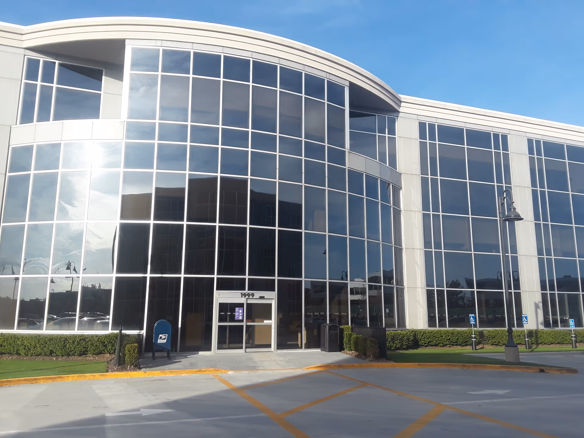 Glass-fronted modern medical center with curved facade and entrance, parking lot in foreground.