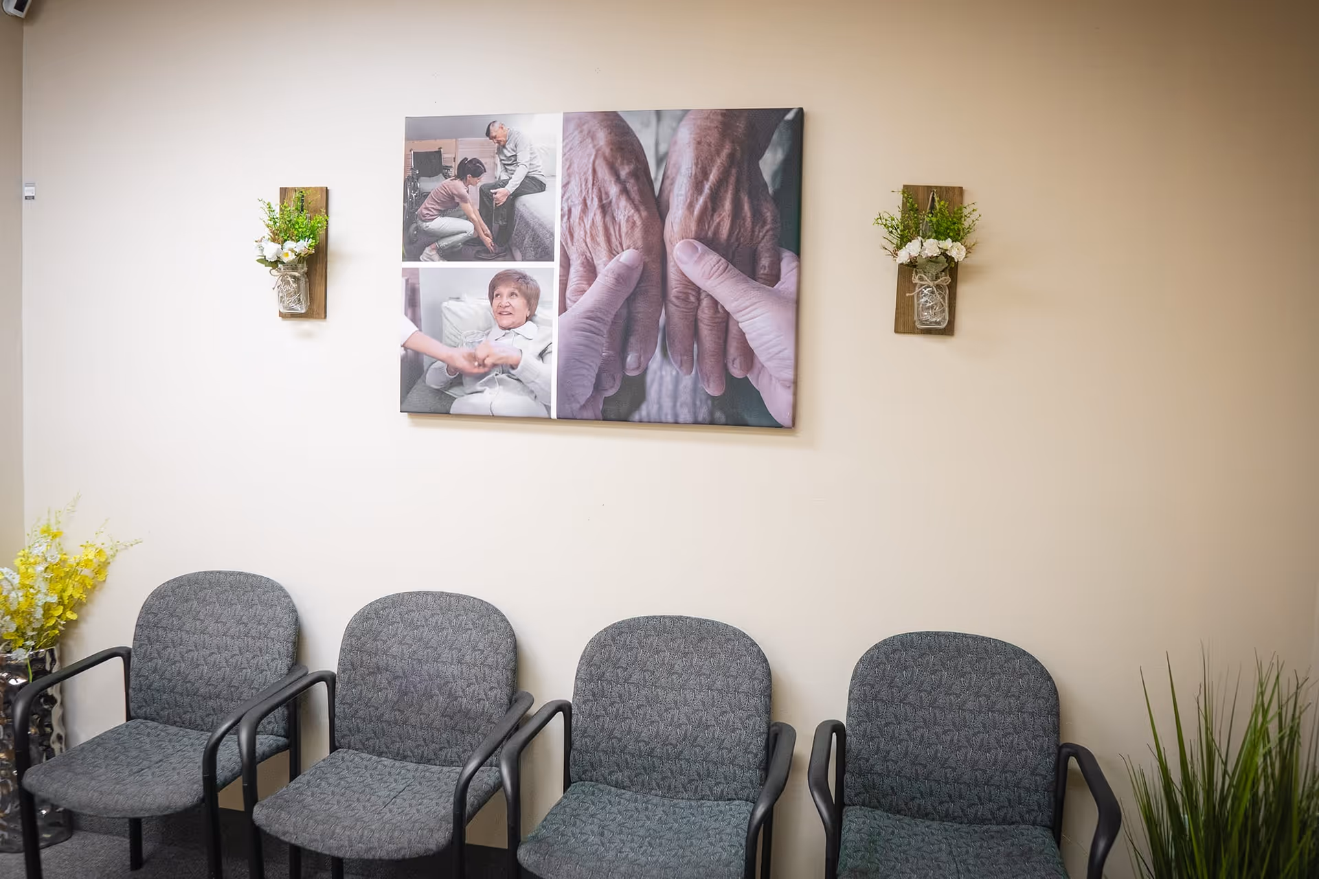 Row of gray chairs along a beige wall with artwork and plants.
