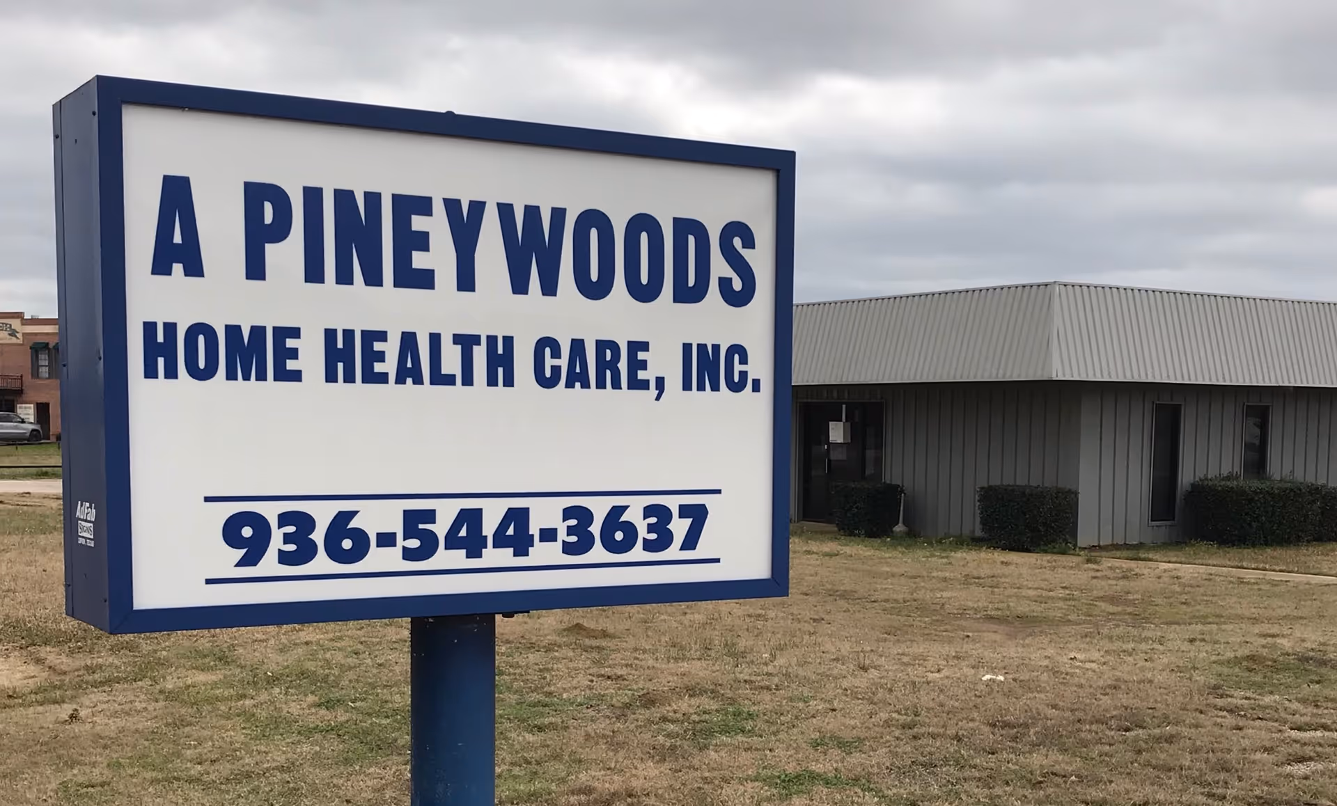 Front view of a large sign advertising A Pineywoods Home Health Care, Inc., with a building.
