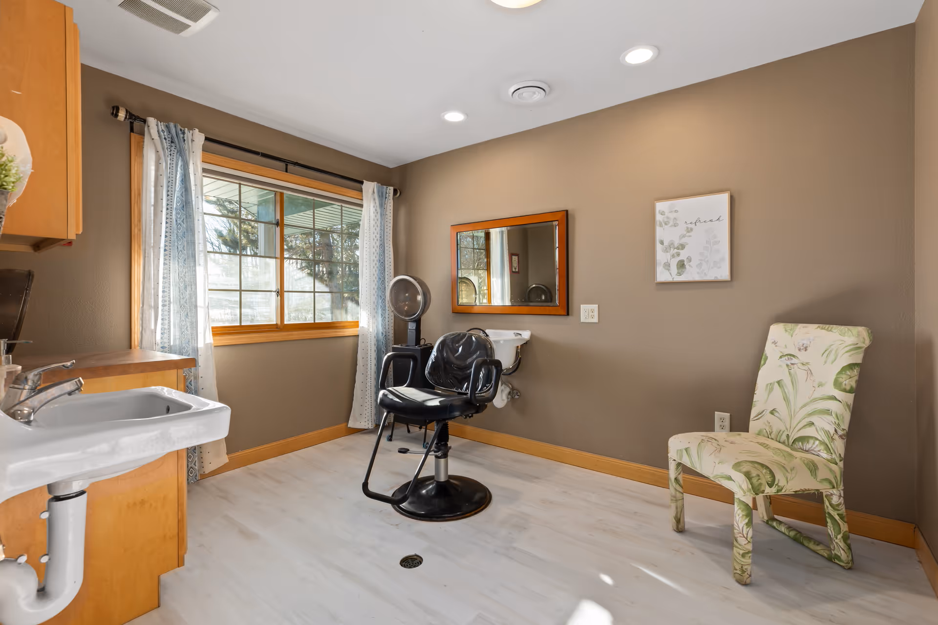Hair salon area with chair, sink, mirror, window, and patterned accent chair.