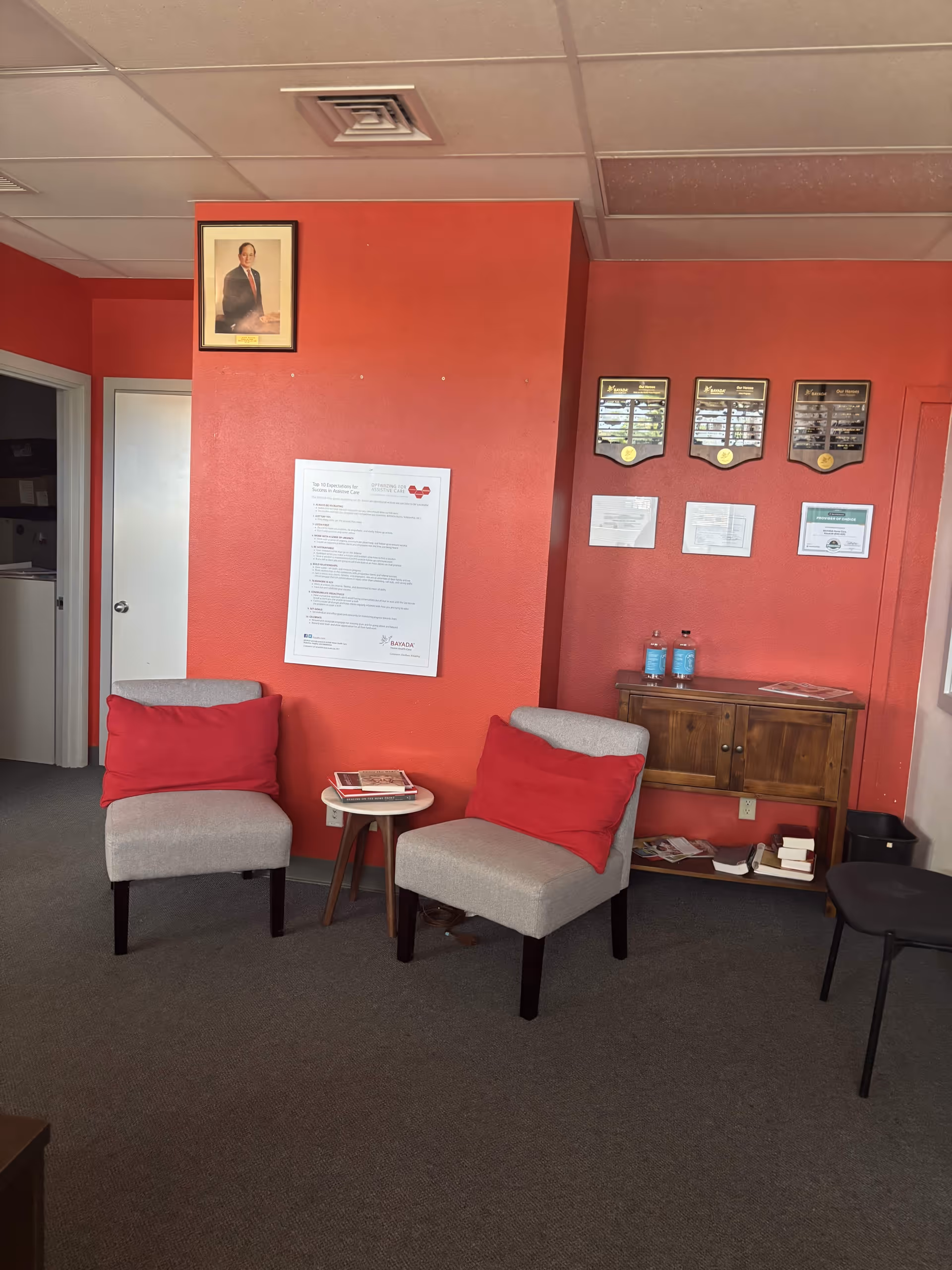 Red-walled lounge area with two gray chairs, red cushions, a small table, and wall plaques.