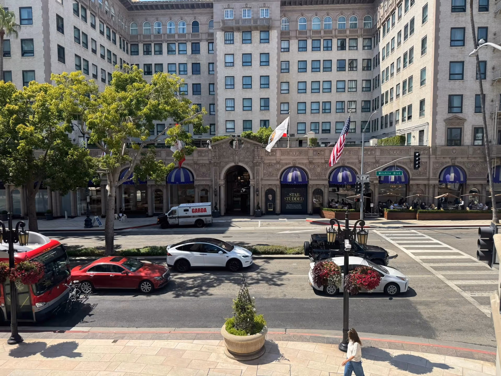 Grand stone building façade with arches, flags, trees, and traffic along a city street.
