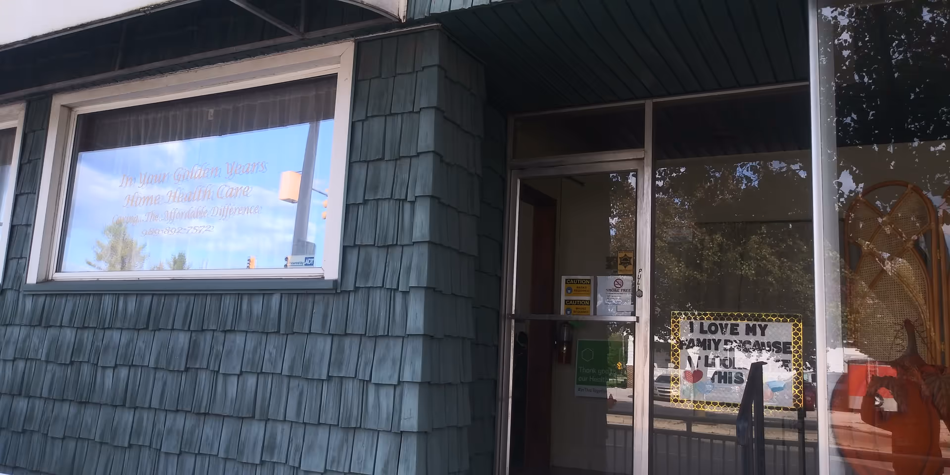 Exterior of a senior living facility with teal siding and a glass entry door.