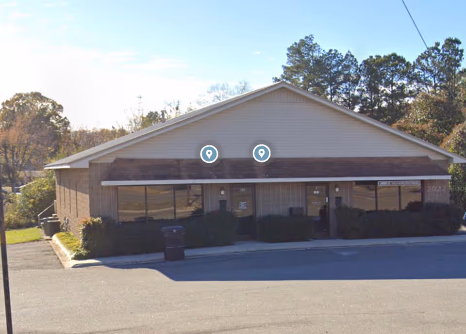 Single-story, brown-brick senior living facility with front windows and a paved driveway.