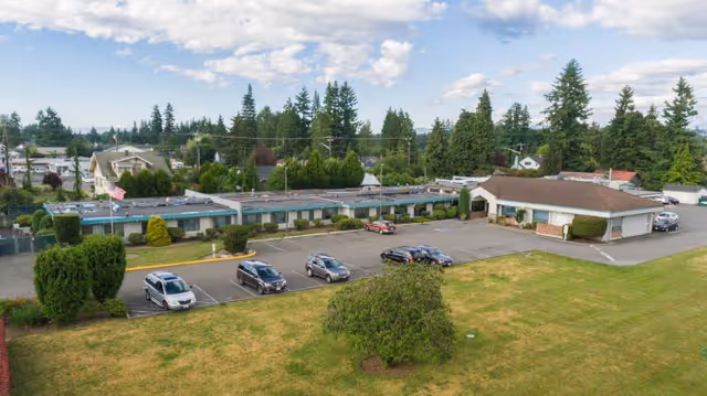 Aerial view of a single-story rehabilitation and care center with a parking lot, grassy lawn, and surrounding trees.