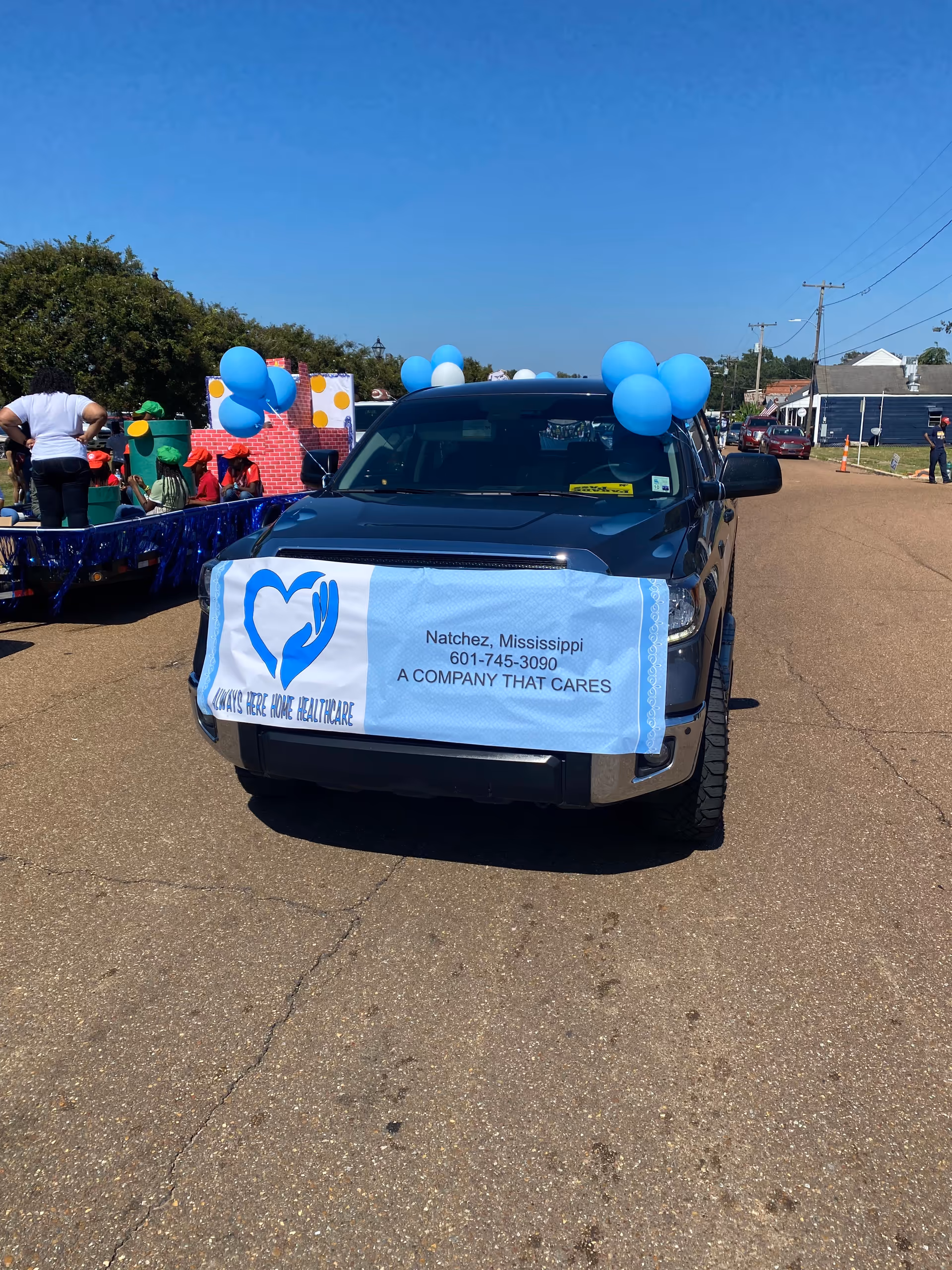 Truck displays Always Here Personal Care Services banner with balloons at an outdoor parade.