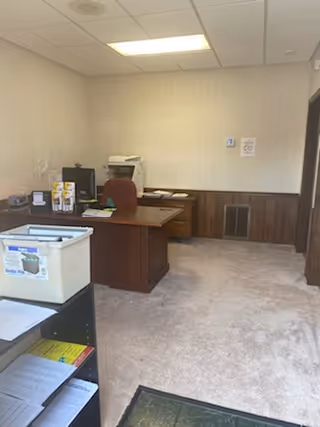 Interior office/reception area with desk, chair, printer, and storage in a neutral room.