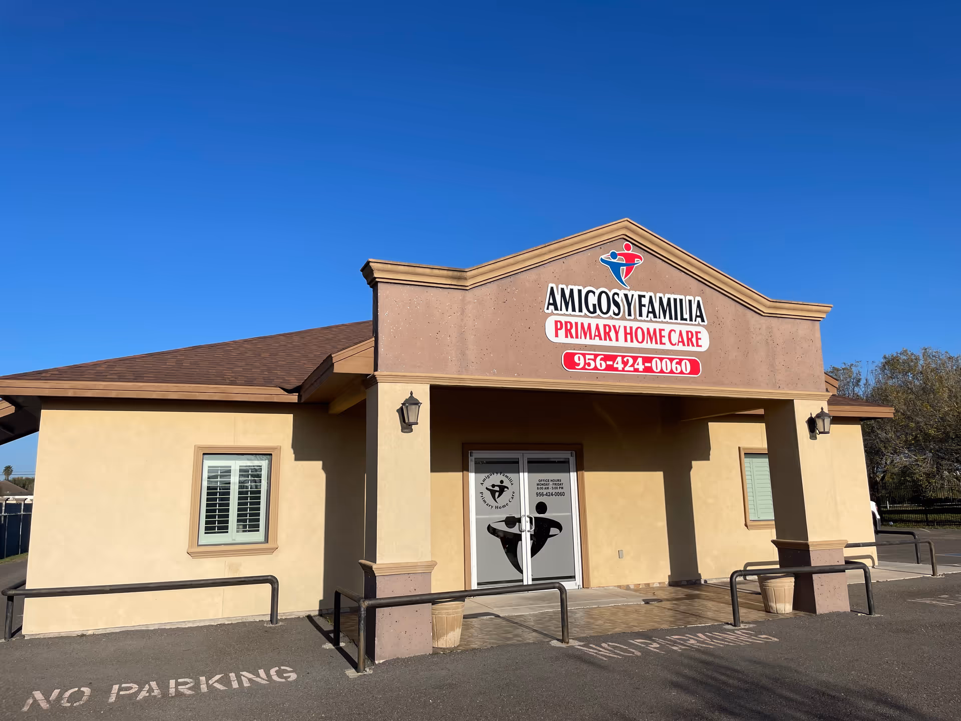 Front view of Amigos Y Familia facility exterior with entry doors and clear blue sky.