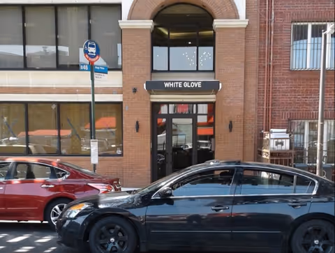 Exterior view of White Glove entrance in a brick building with cars parked outside.