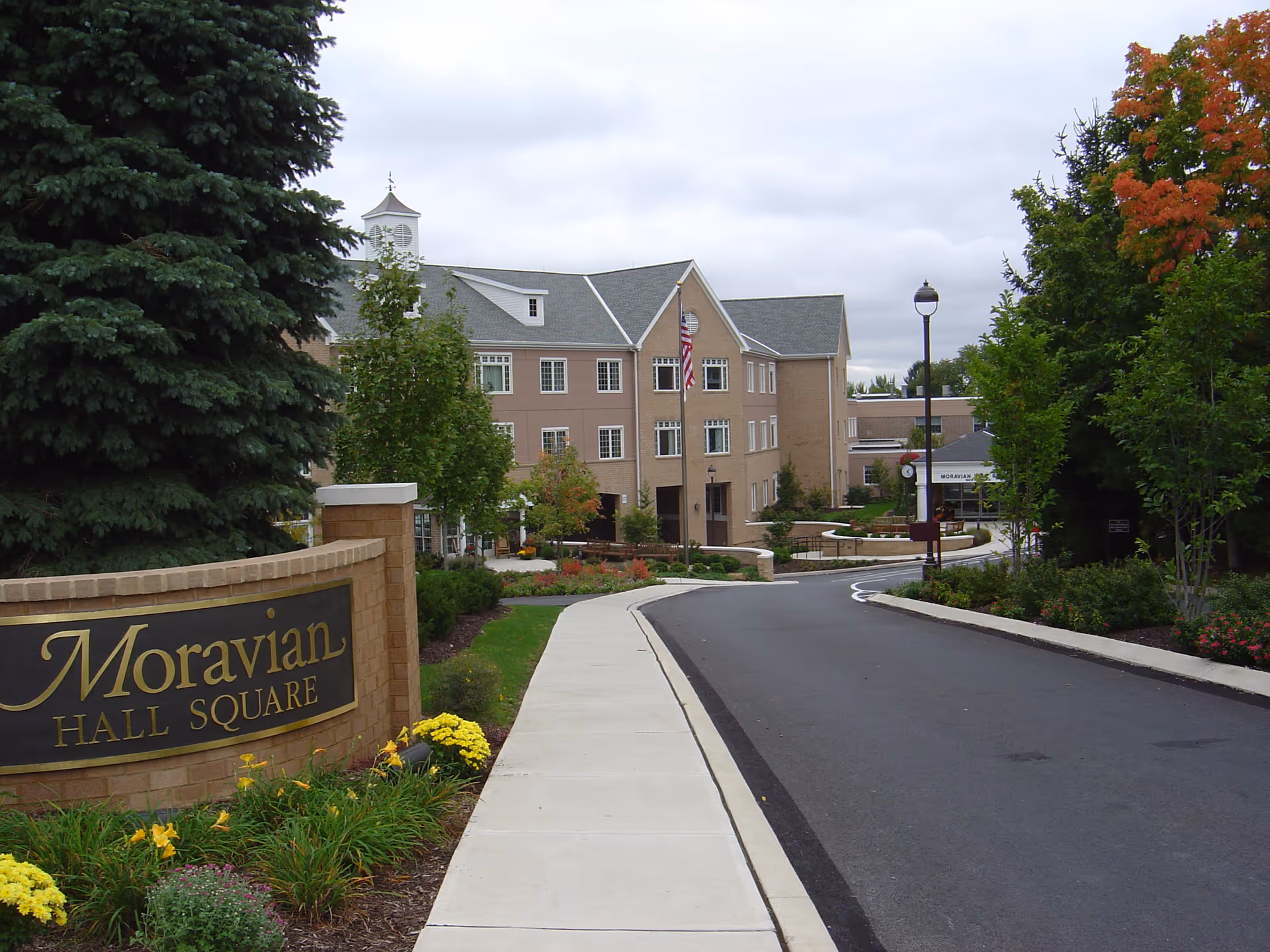 Driveway and landscaped entrance to the Moravian Hall Square building with a large sign, sidewalks, and a multi-story brick facade.