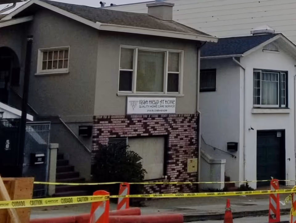 Exterior of a two-story building with Irish Help At Home sign and caution tape.