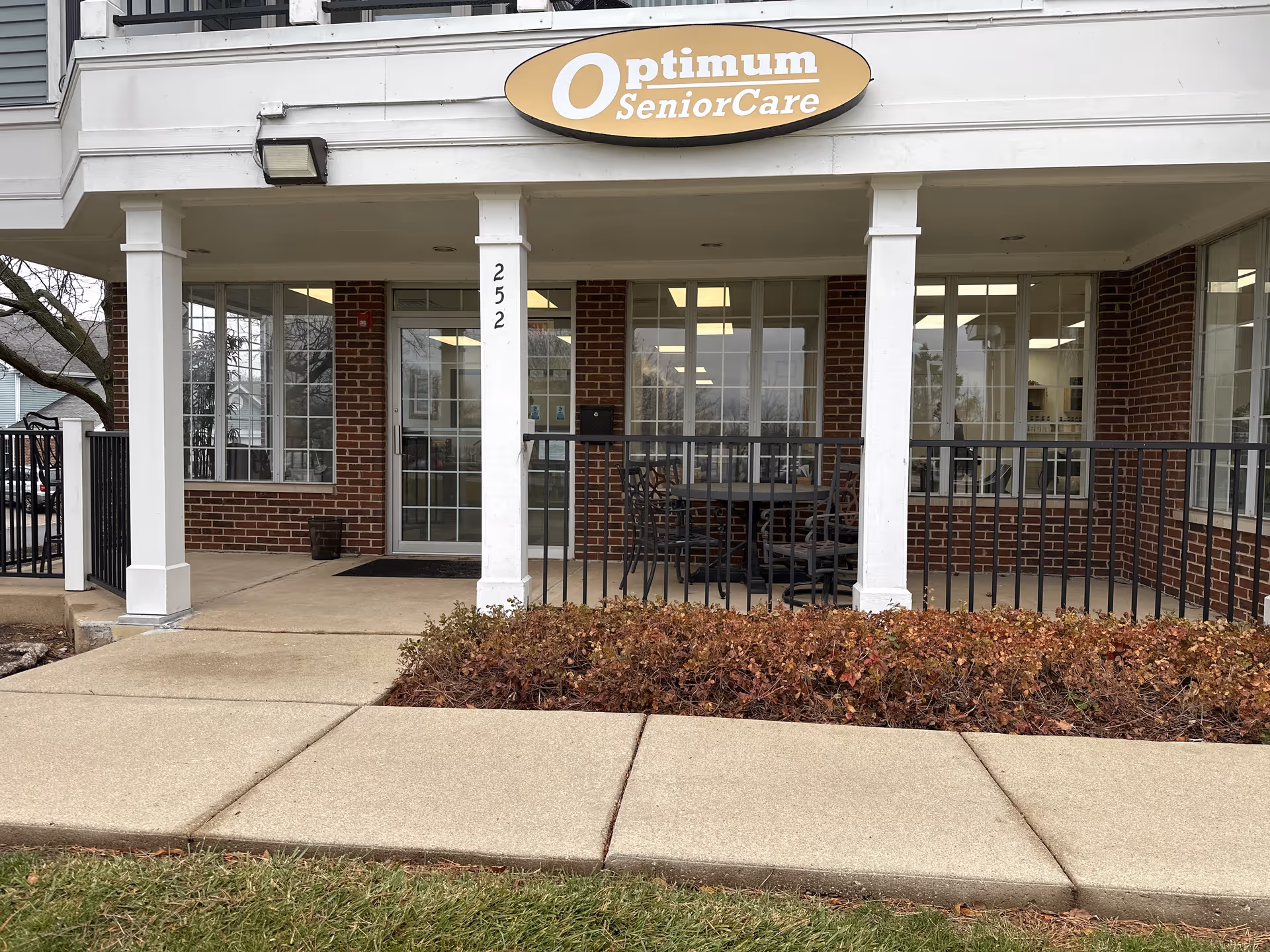Front exterior of Optimum SeniorCare building with a covered entrance and patio seating