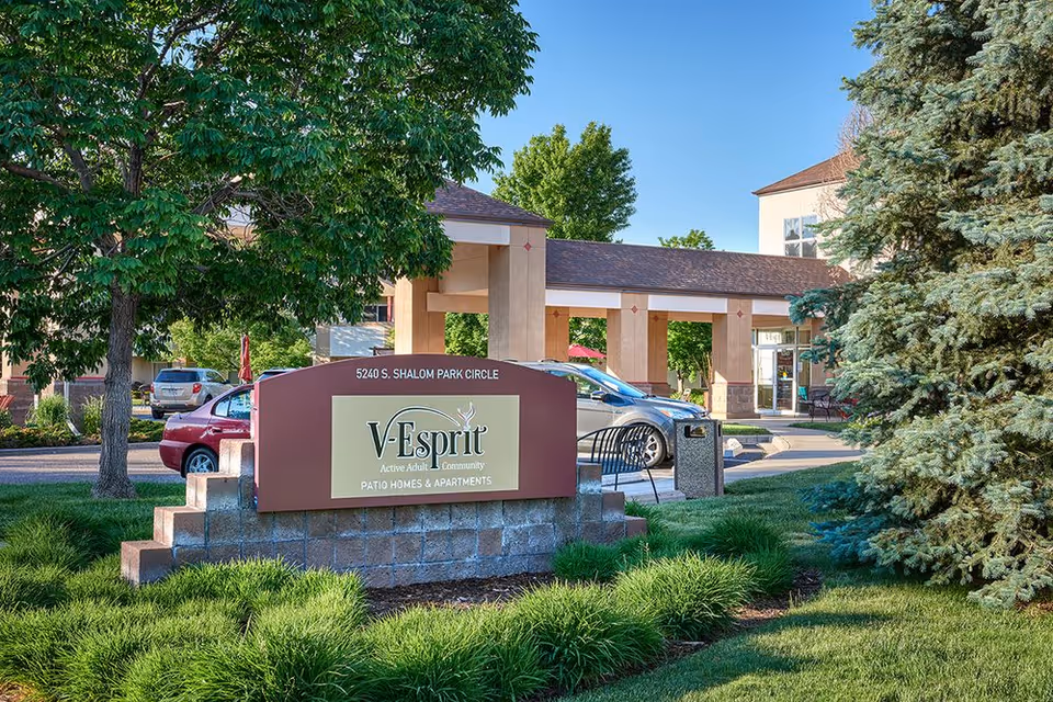 Exterior view of V-Esprit facility with sign, entrance, trees, and parked cars.