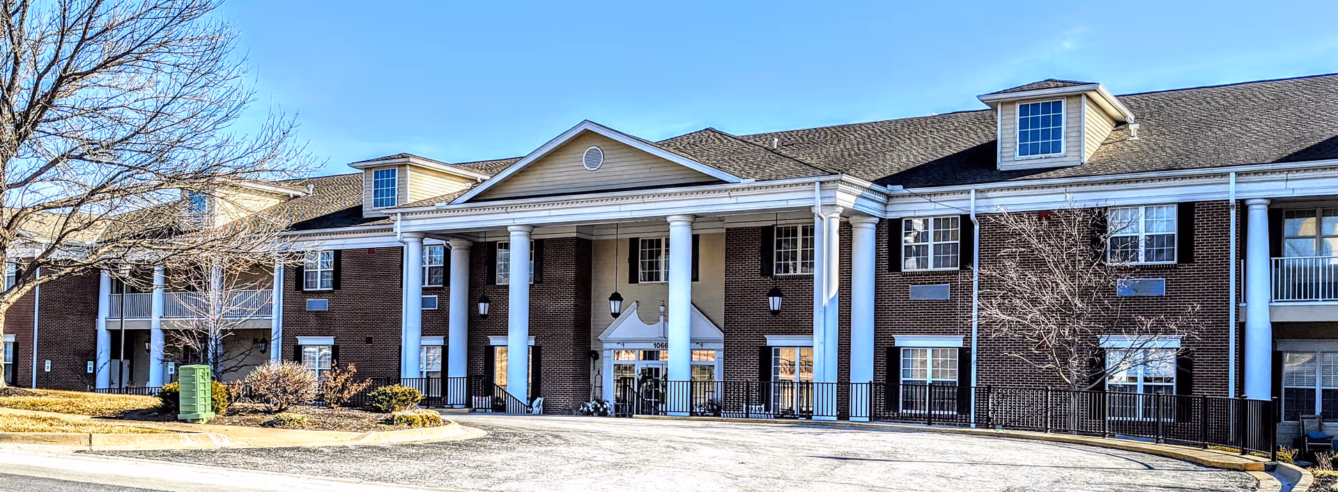 Brick senior living building with white columns and a central glass entrance under a clear sky