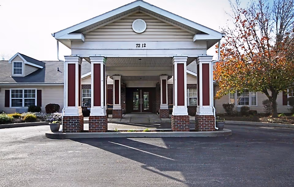 Exterior shot of a senior living facility entrance with a covered drive and brick columns.